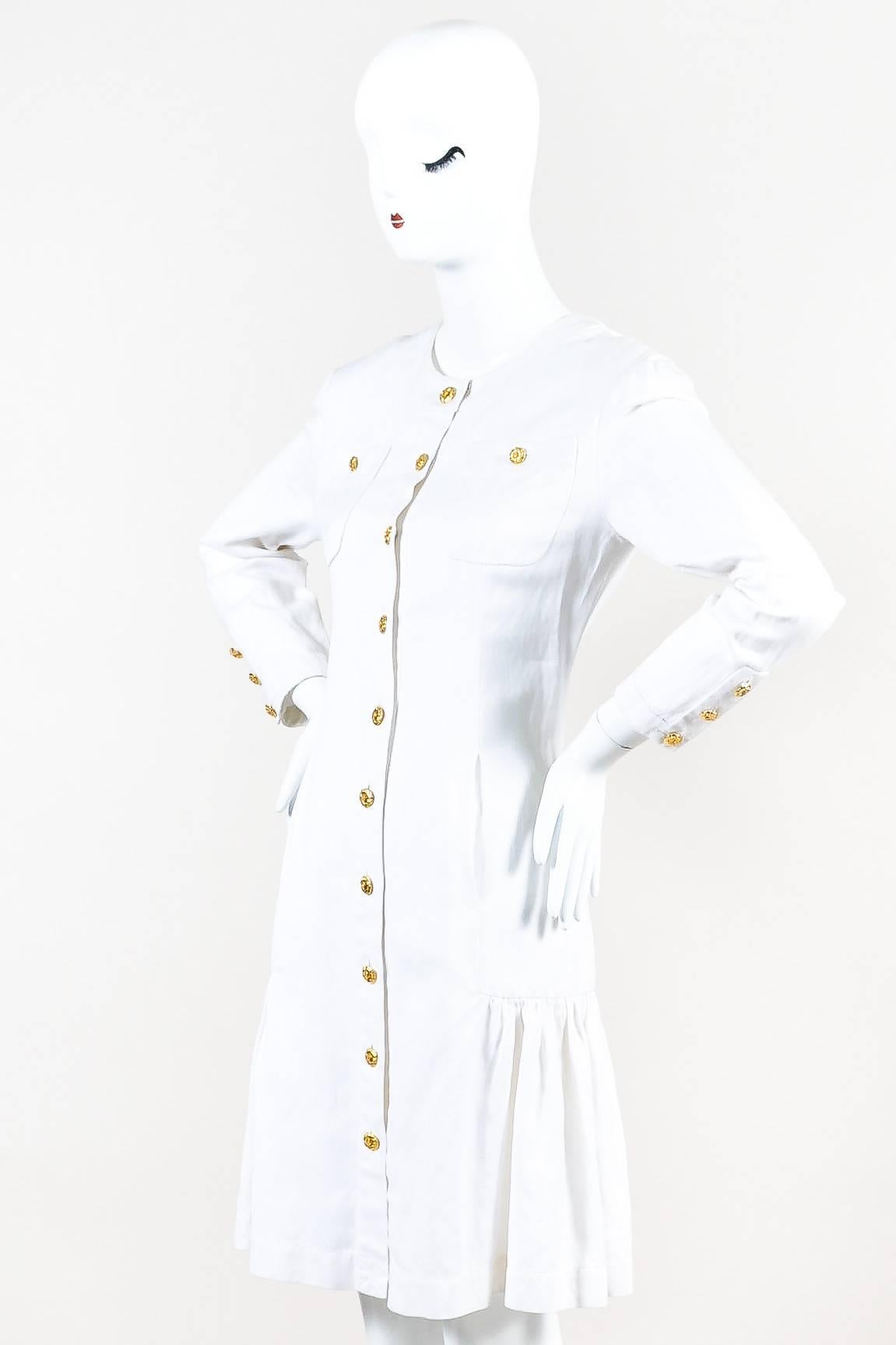 This clean and fresh long sleeve dress from Chanel features button closures at each opening. Padded shoulders. Beautiful gold flower shaped button closure down front. Pockets at each lapel with button closure on top of each. Dropwaisted style with