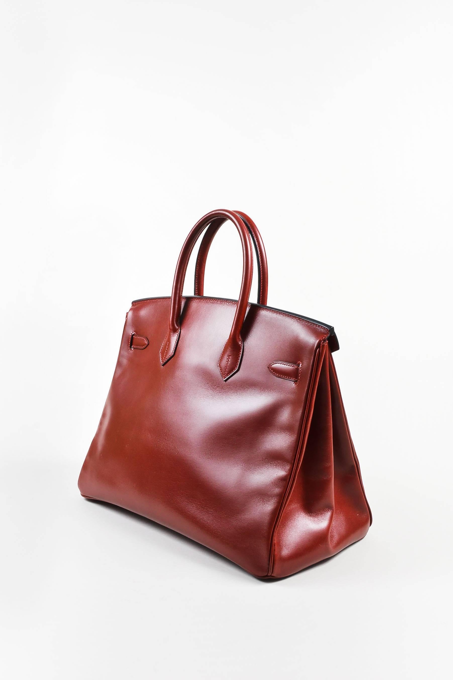 Comes in dust bag. Circa 2001. This 35cm size Birkin handbag is constructed of rich oxblood red box calf leather with gold-tone metal hardware. Two rolled top handles. Front straps secure with a padlock to close the main turn lock. Comes with two