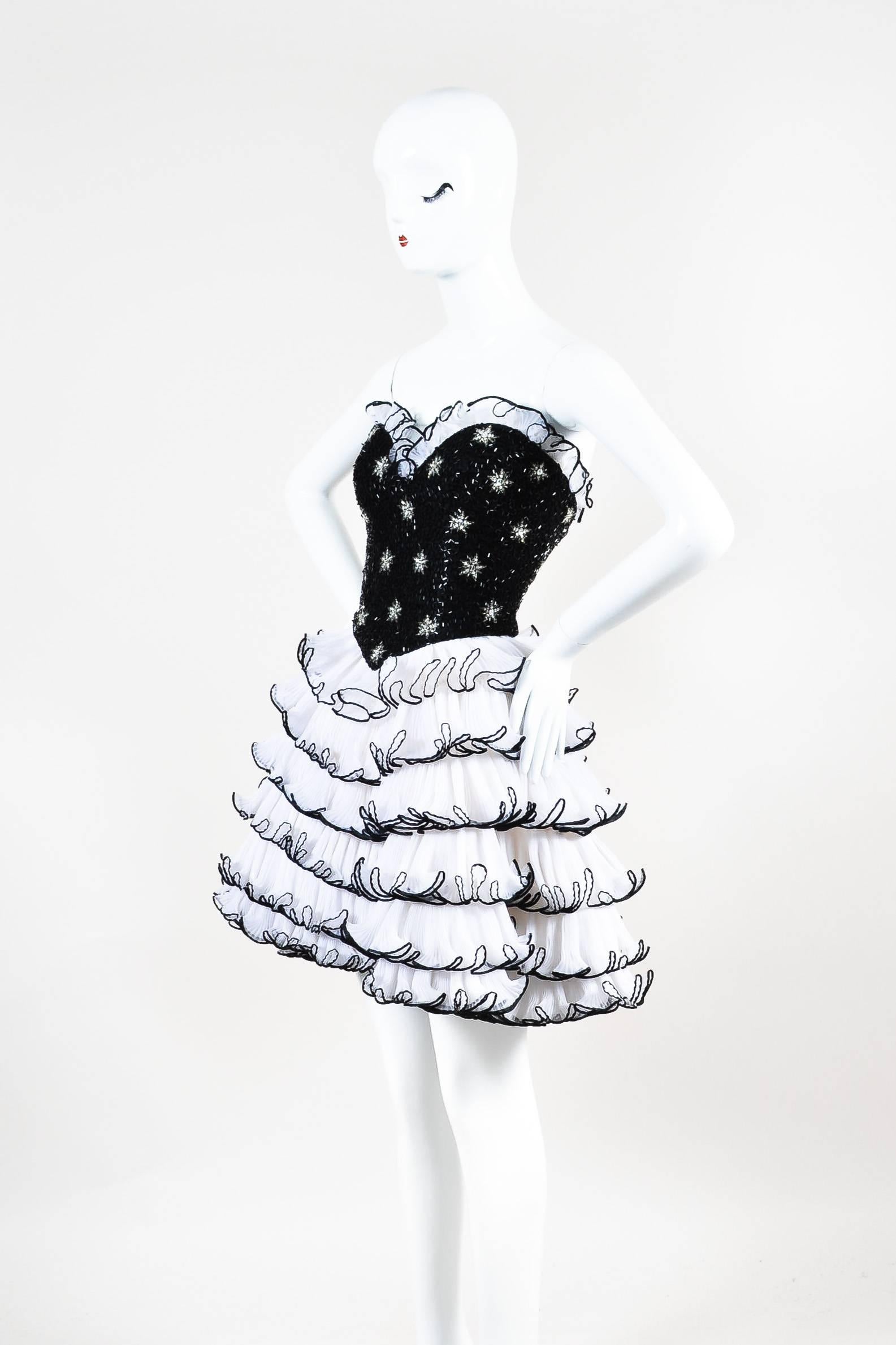 Short strapless cocktail dress. Sweetheart neckline. Black bugle beads and silver sequin embellishment throughout fitted bodice. Layered and tiered accordion-pleated cream ruffles with black trim throughout skirt; same ruffle trim at bust. Light