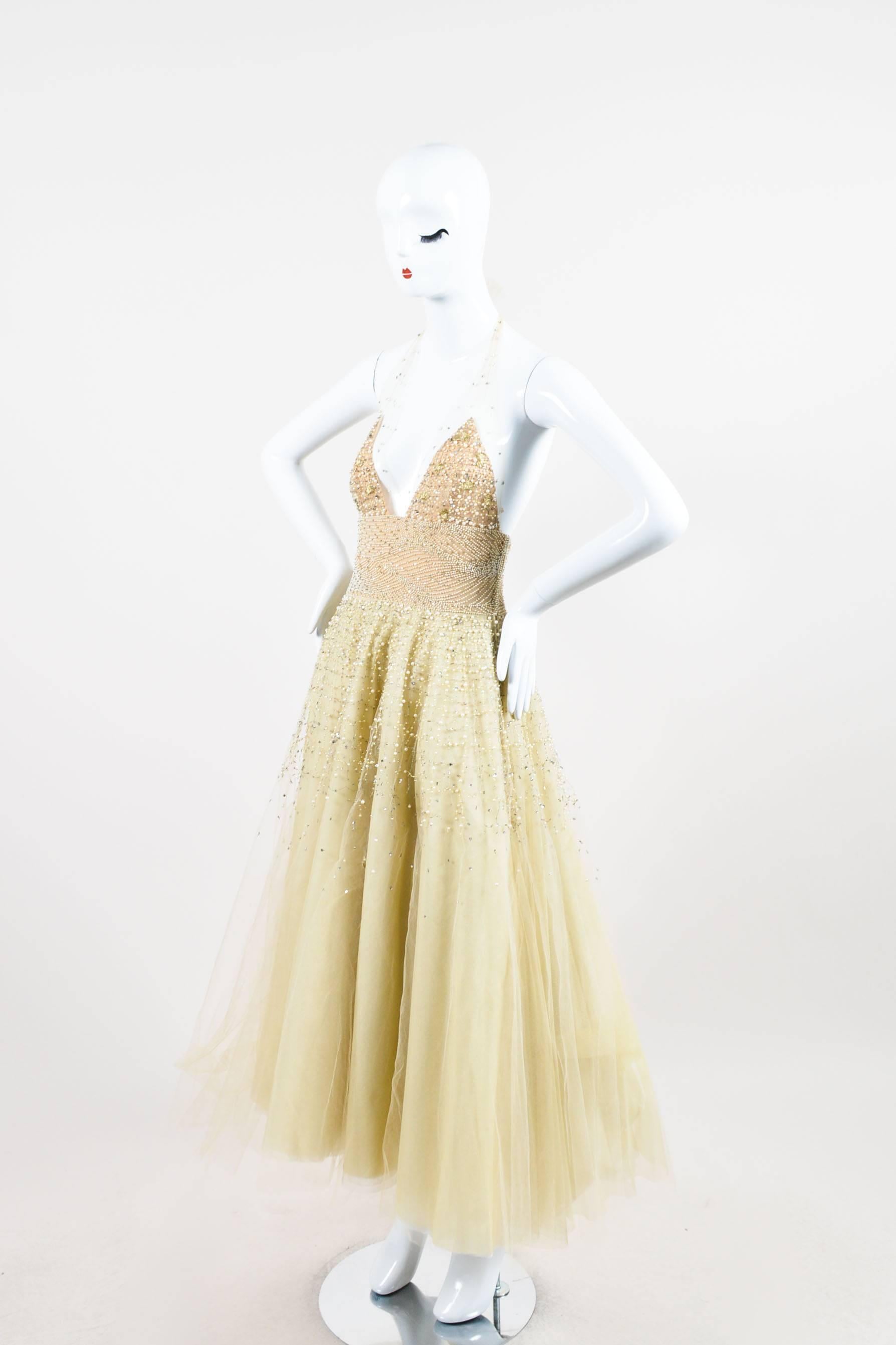 Romantic pale yellow tulle evening gown with silver-tone beads and sequins, faux pearls, and metallic silver and gold embroidery. Halter neckline with adjustable tie for desired fit. V-neckline. Full, layered tulle skirt. Beige lining at bodice.