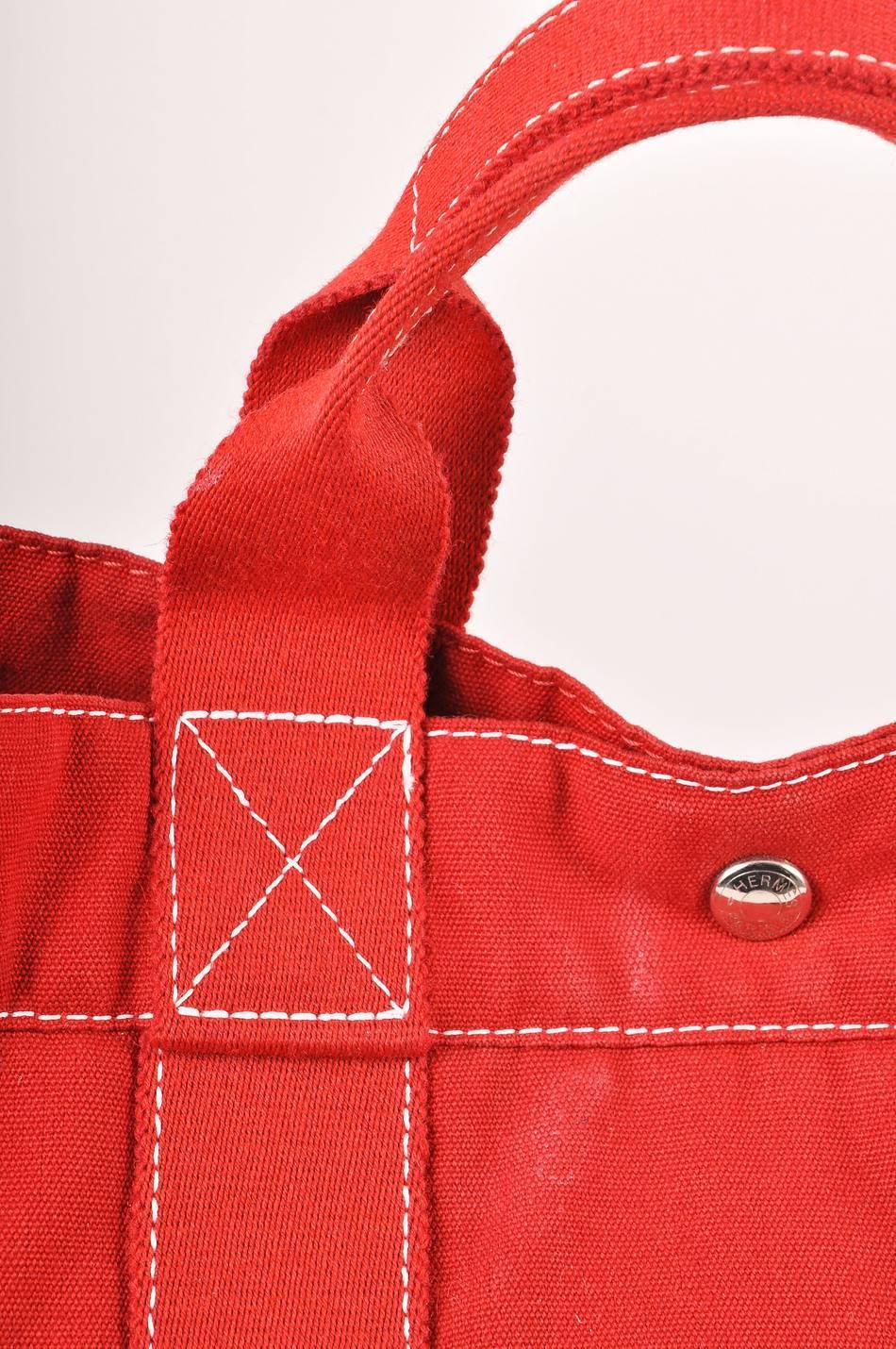 Red canvas beach tote has white stitching details throughout. Three flat pockets along each side. Two flat handles and snap closure at top. One large zipper pocket inside.

Additional Measurements:
Handle length: 11
