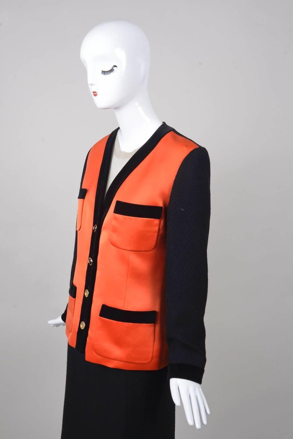 This vinage CHANEL jacket features long knit sleeves with a knit back panel.
Front panels are orange satin with black velvet trim around the neckline and front. Four front pockets with matching velvet trim. Gold and black buttons down front with