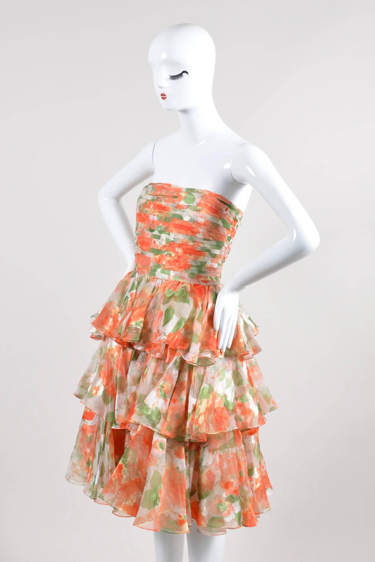 Eye-catching vintage dress by Oscar de la Renta in a bright floral print. Shades of coral orange, green, white, and yellow throughout. Pleated bust area and tiered ruffle skirt. Interior belt for fit and shape. Hits approximately above the knee.