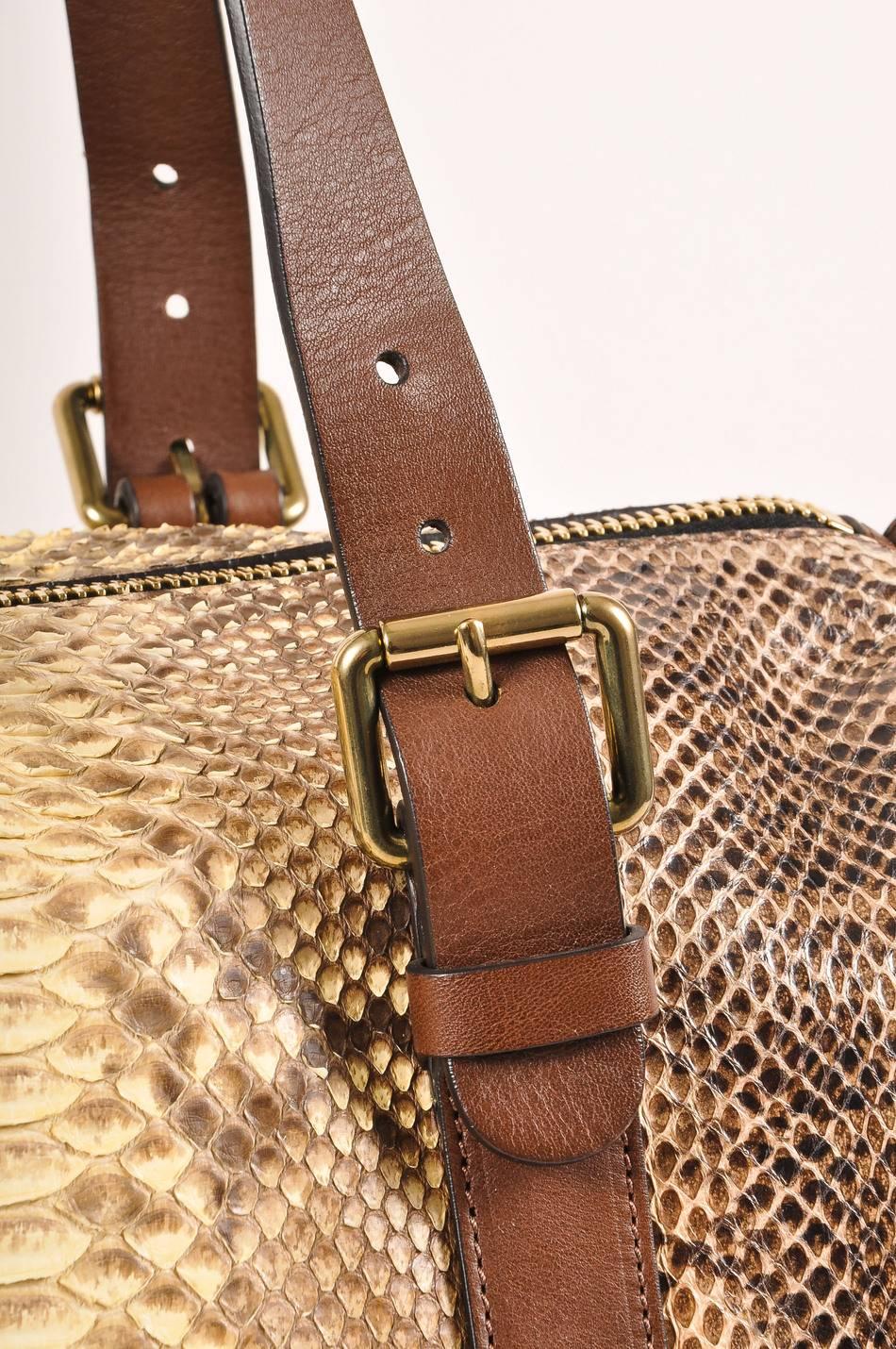 This oversized duffel bag features mixed snakeskin construction; panels of viper, ayers, and python skins. Two flat brown leather handles with gold tone buckles. Optional shoulder strap and tassel detail. Top zipper closure. Black textile lining. To