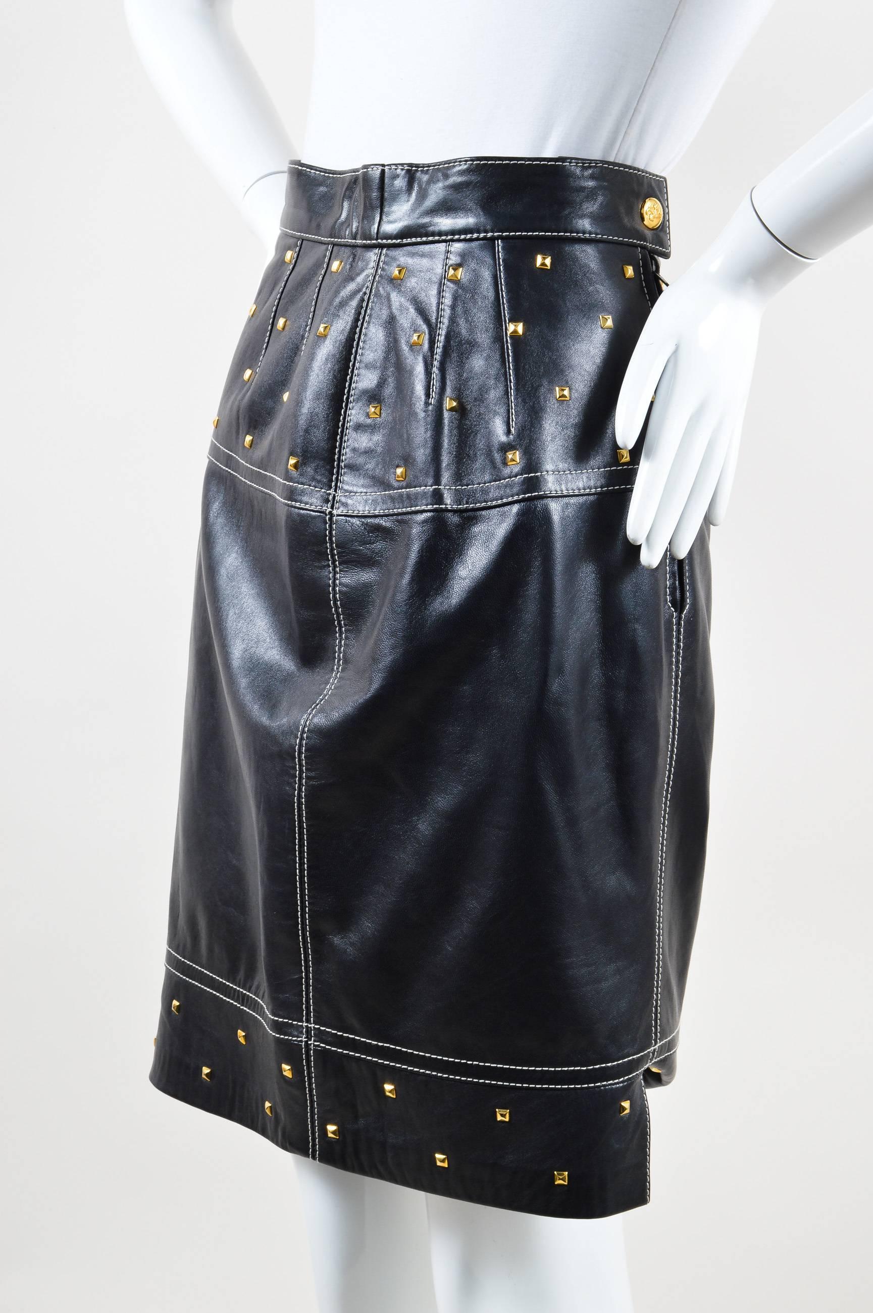 Unique vintage skirt that can be dressed up or down. Smooth, supple leather. Gold-tone pyramid studded embellishment. Contrast white stitching. Hits at knees. Hidden back zip closure. Back snap button closure. Lined. 