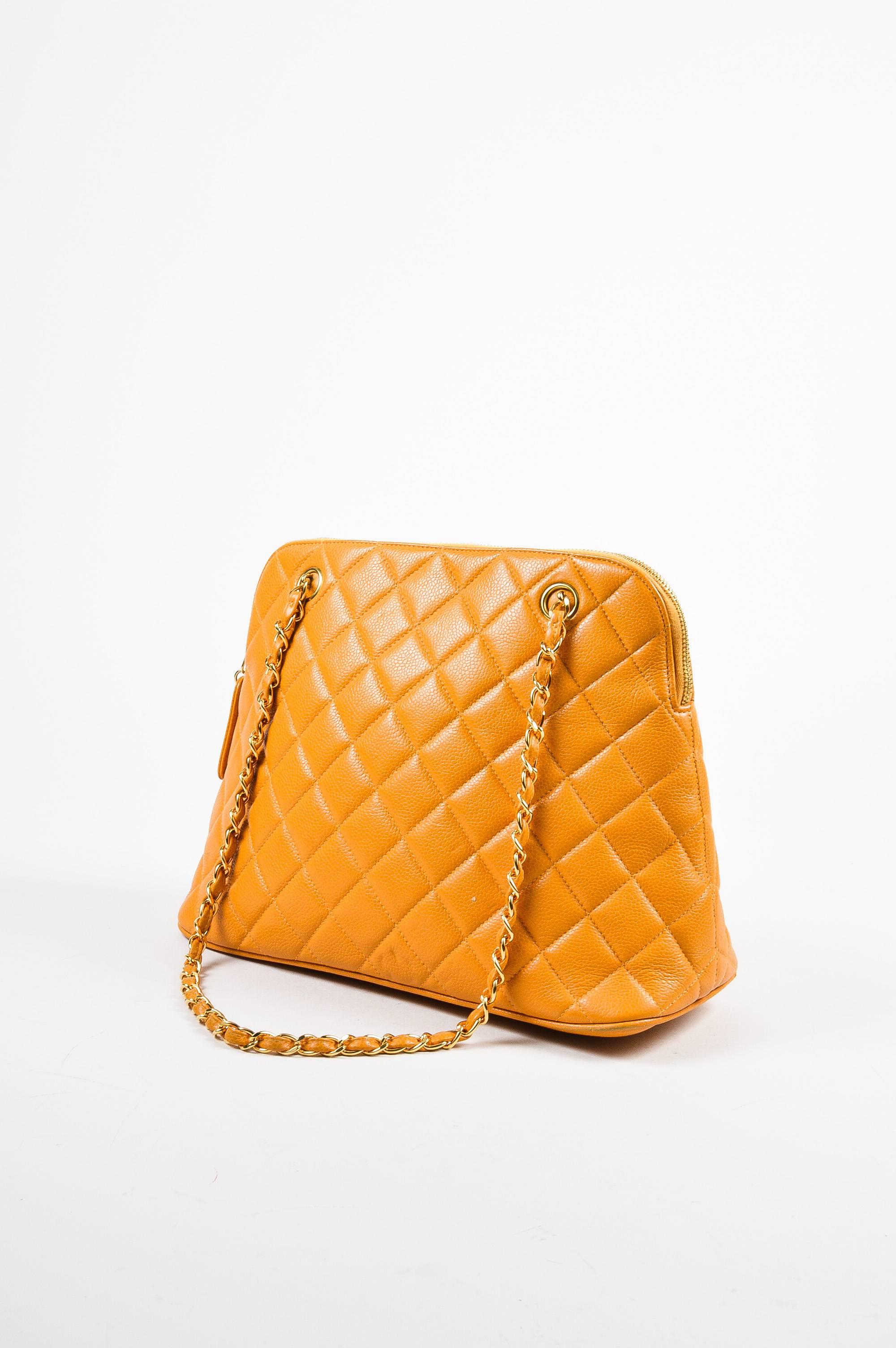 Bright and summery shoulder bag constructed of marigold orange caviar leather bag circa 1996-1997. Diamond-quilting. Gold-tone hardware. Dual chain link shoulder straps with leather weaving. Unexpected 'CC' stitched logo on base. Zips closed around