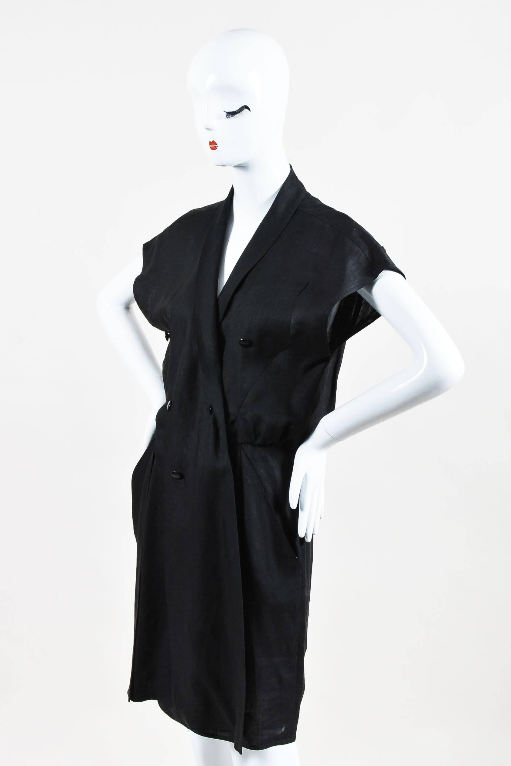 Vintage black linen dress has button closure and details in front. Loose fitting cap sleeves. Single lapel pocket. Skirt has two draped tie embellishments hanging over front with zip fly and button closure underneath. Slanted side