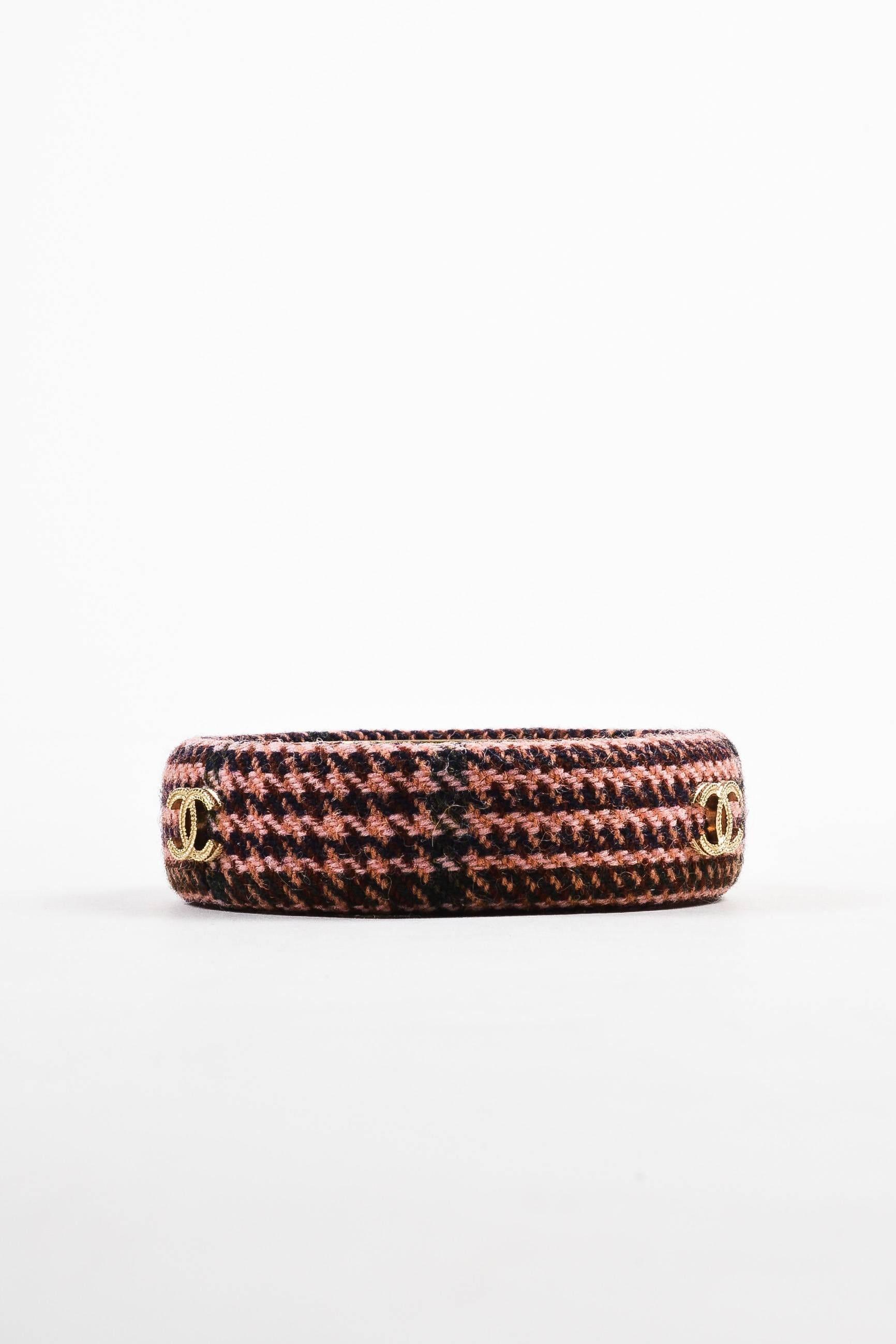 	
From the Fall 2013 collection. Retailed for $650. This stylish bangle pays homage to Chanel's iconic tweed jackets. Constructed of woven wool in shades of pink and brown. Three gold-tone metal 'CC' logos adorn exterior. Smooth metal