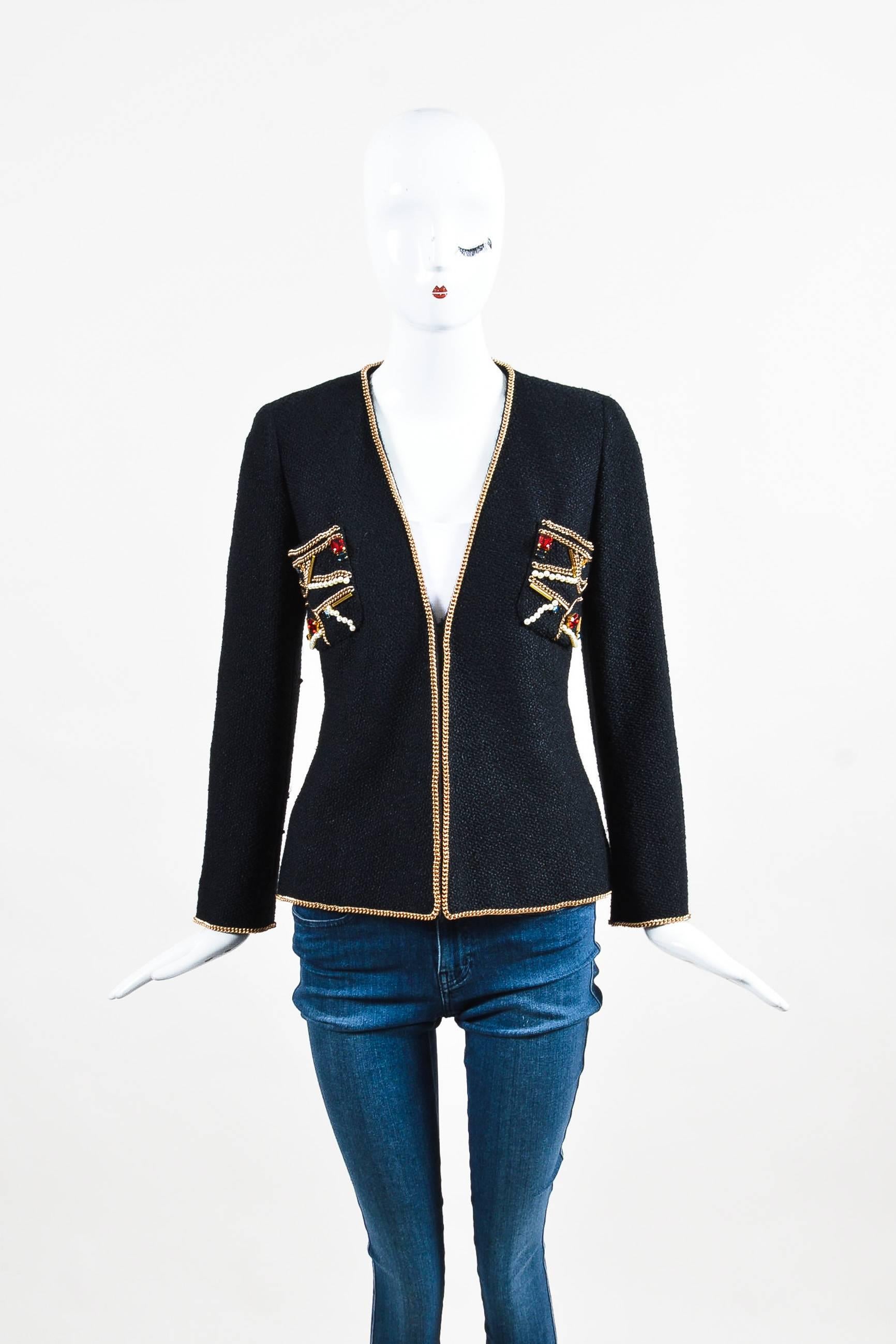 This elegant and classic jacket by Chanel that is the perfect addition to any wardrobe. Black tweed material with embellishments at the front. Chain trims with faux pearls and gems in red nad blue hues. Single hook-and-eye closure at the front with