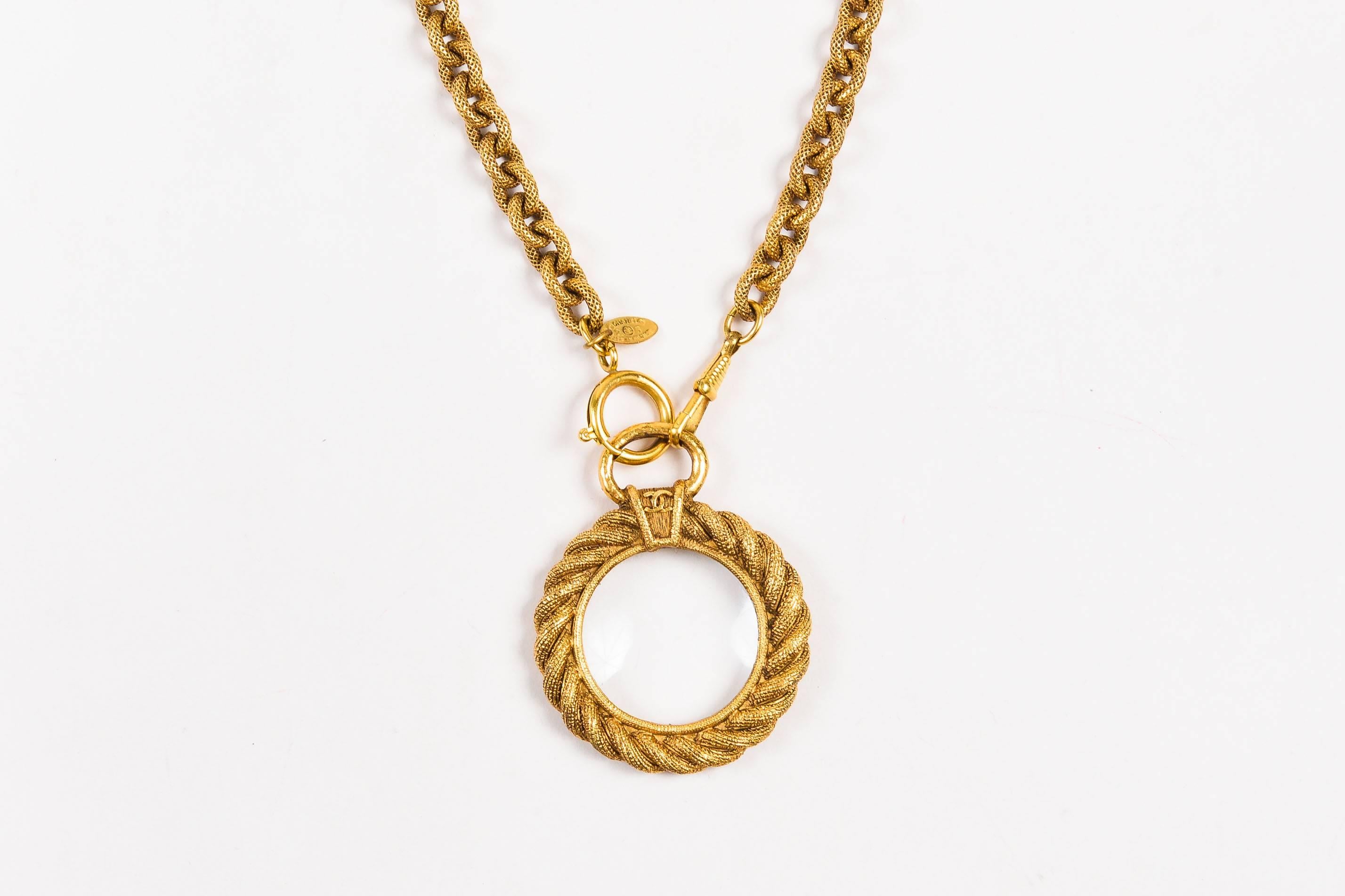 Add vintage sophistication to your closet with this unique necklace. Gold-tone metal construction. Rolo link chain with intricate etched detail. Round magnifying glass pendant with woven border. Lobster clasp and spring clasp at ends of