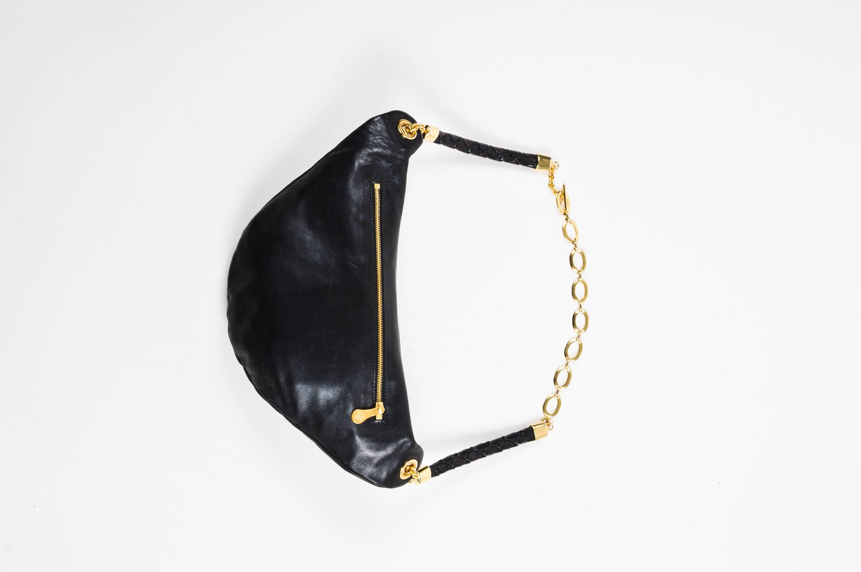 A fashionable fanny pack constructed of supple black leather and accented with shiny gold-tone hardware. Crescent shaped bag features embroidered detailing, a front zip compartment, and a hidden back zip pocket. Chain link and braided leather strap.