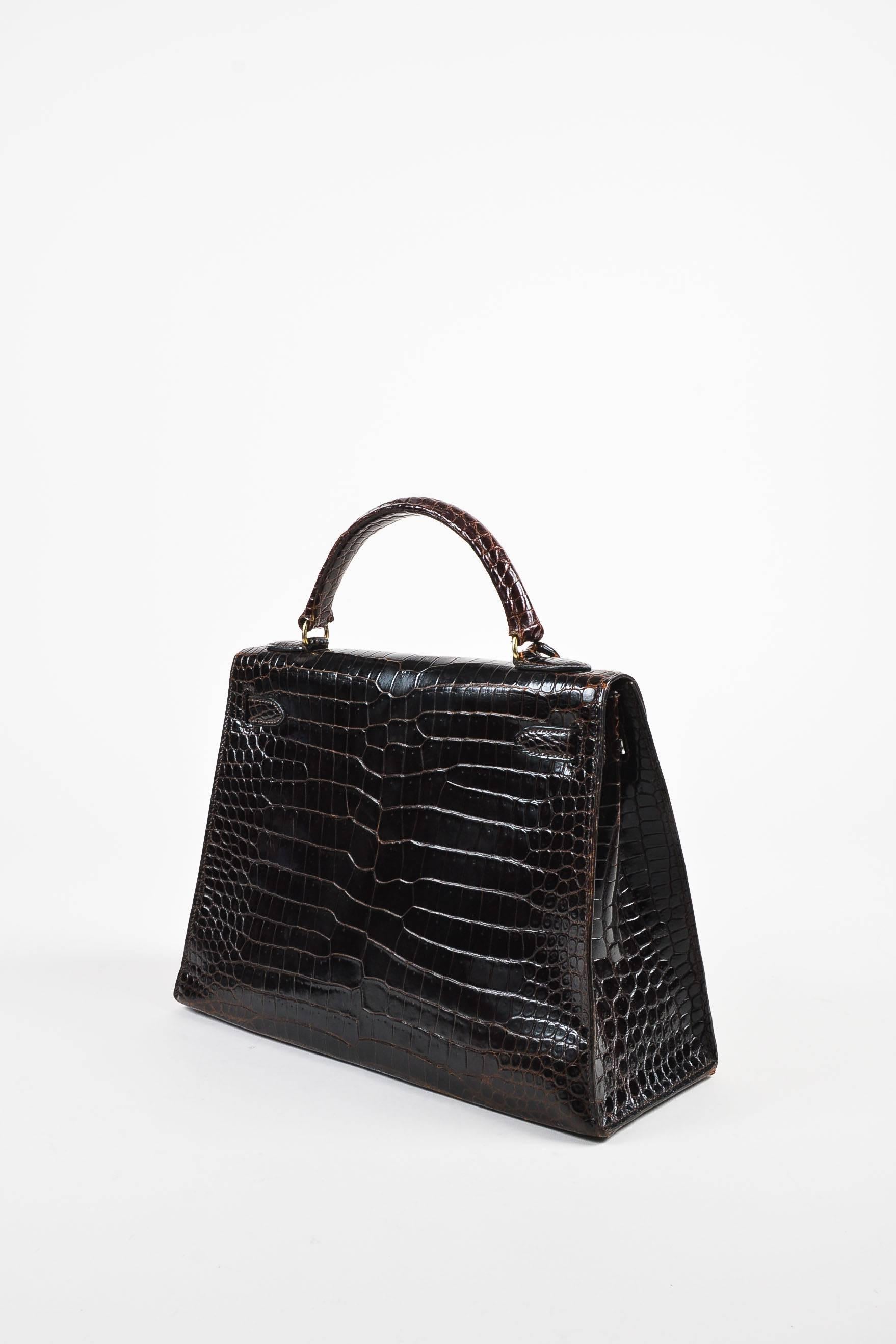 A classic and chic purse that is perfect for any collector or enthusiast. This "Kelly 32" bag by Hermes features a luxurious, brown, Porosus Shiny crocodile construction with gold plated hardware. Sturdy, box shape with a flat base and