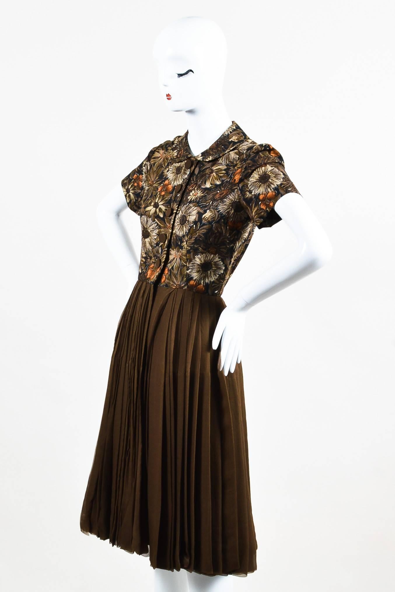 Vintage collared short sleeve button down dress from Henri Bendel. Rounded collar. Buttons down the front of shirt for closure. Navy, brown, and burnt orange floral print on the shirt. Zipper on the upper portion of skirt. Olive green pleated skirt.