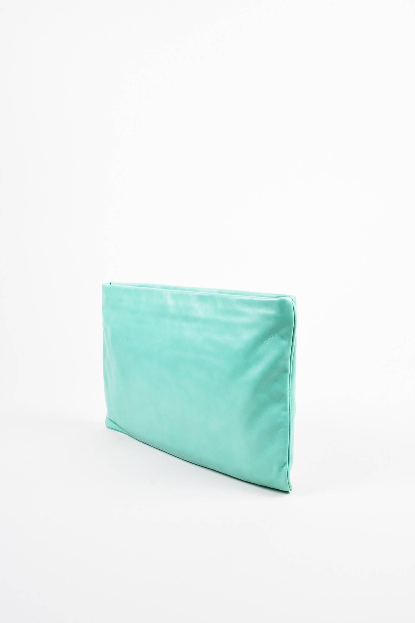 Turquoise leather clutch bag by Prada featuring red and white dice at front corner, trimmed in black patent leather . Designed with a gold-tone metal zip closure. 