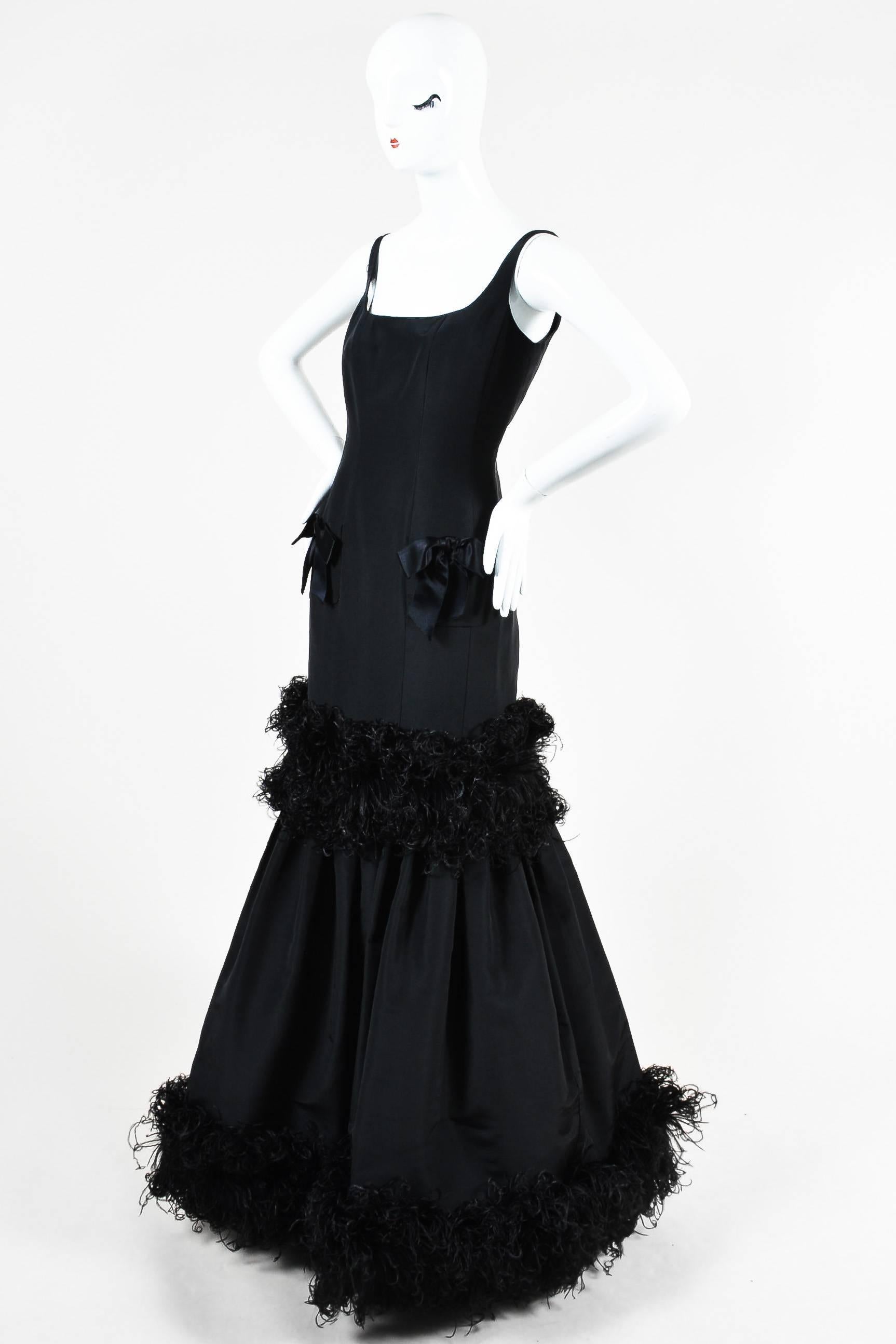 Dazzle at your next event by pairing this evening gown with sparking jewels. Constructed of black silk taffeta. Figure flattering mermaid silhouette. Feather trim appears to be genuine ostrich feathers. Front pockets detailed with satin bows. Square
