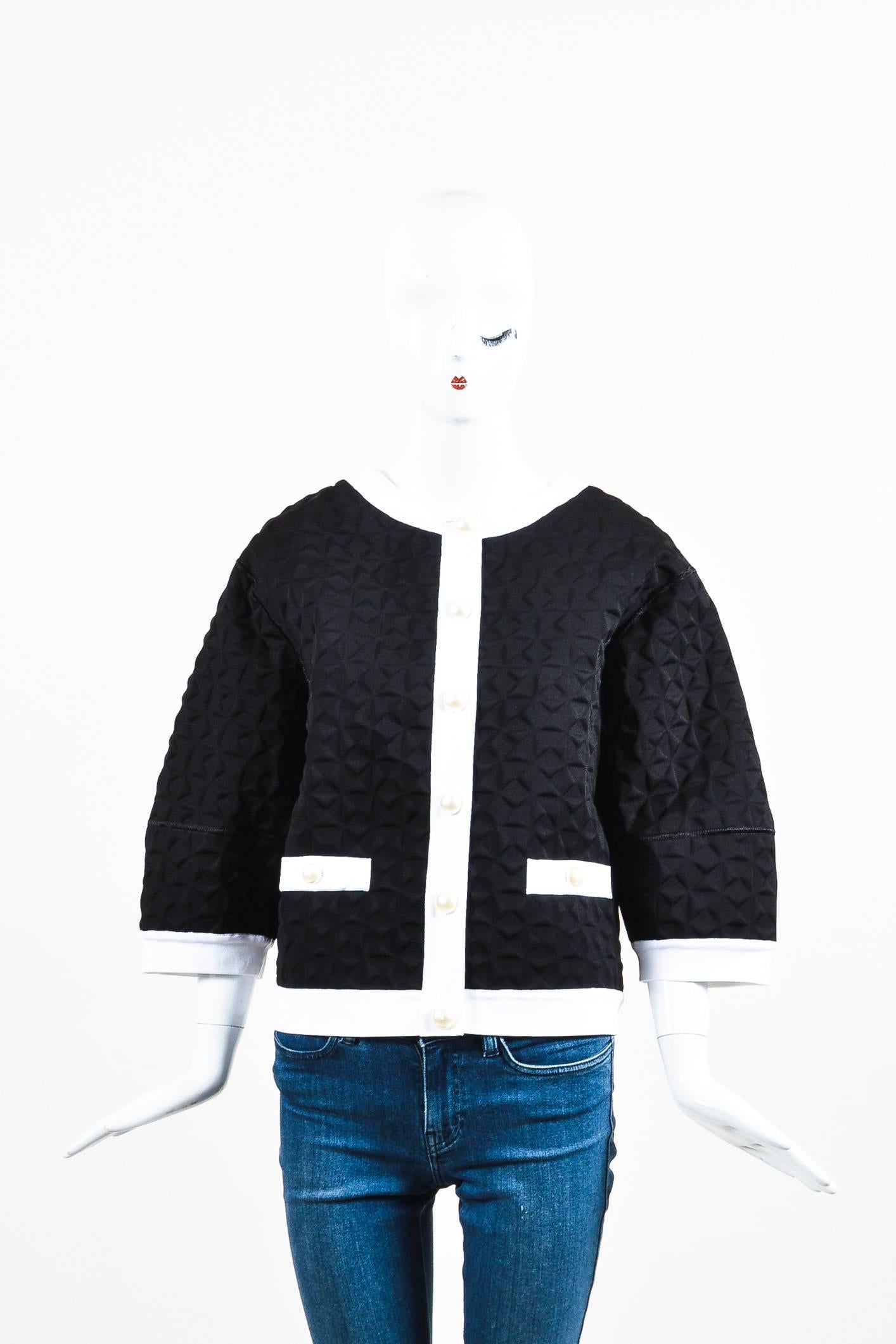 Retails for $4245. Chic and modern Chanel jacket in a textured design. Black and white colorway with a stiff material and ribbed trims. Cropped sleeves with drop shoulders. Faux pearl buttons at the front closure and pockets. Relaxed, boxy shape.