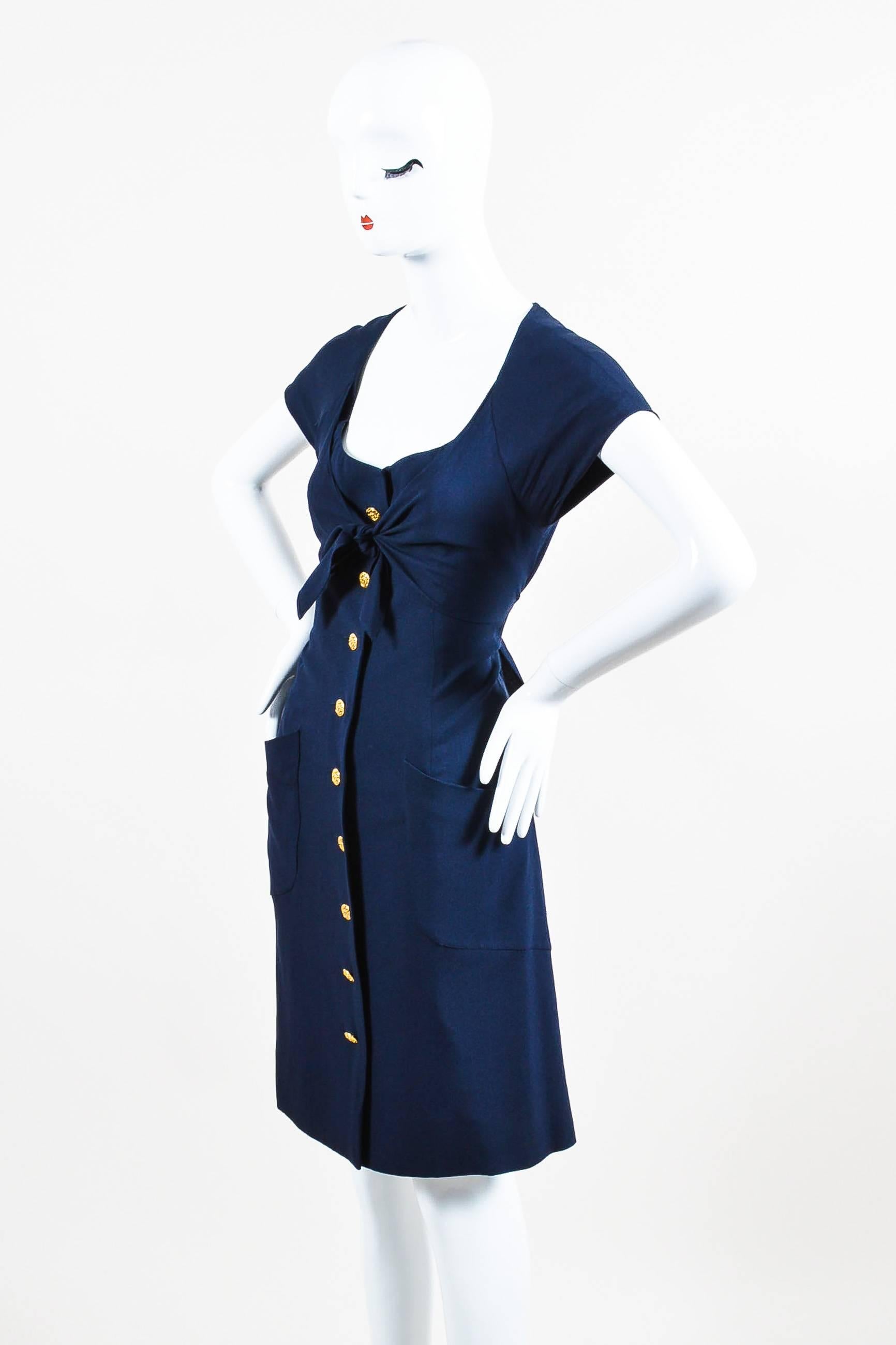 Sailor-chic dress by Chanel in a flowing material. This navy blue and gold-tone piece features a button front closure and ruffled trim at the sides. Scoop neckline with cap sleeves. Two front patch pockets. Shift shape hits approximately at the