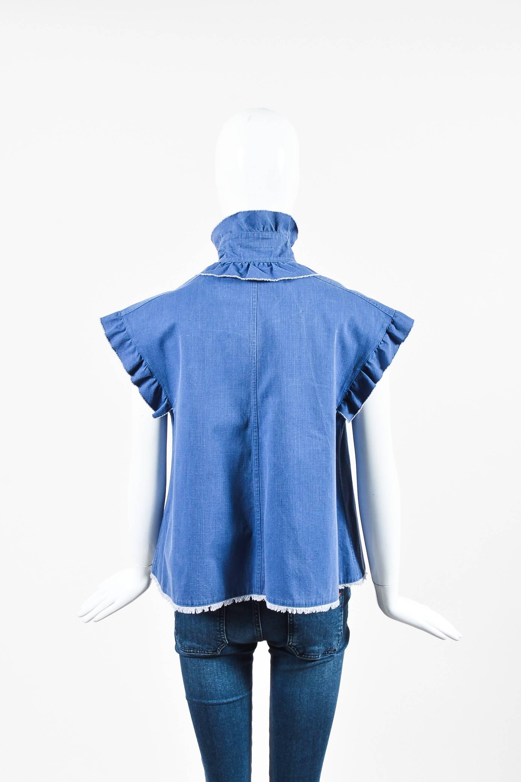 Chanel 07C blue cotton denim A-line blouse featuring ruffle trim along collar, placket, and sleeves. Center front button closures are designed with a navy blue enamel center and silver-tone metal 