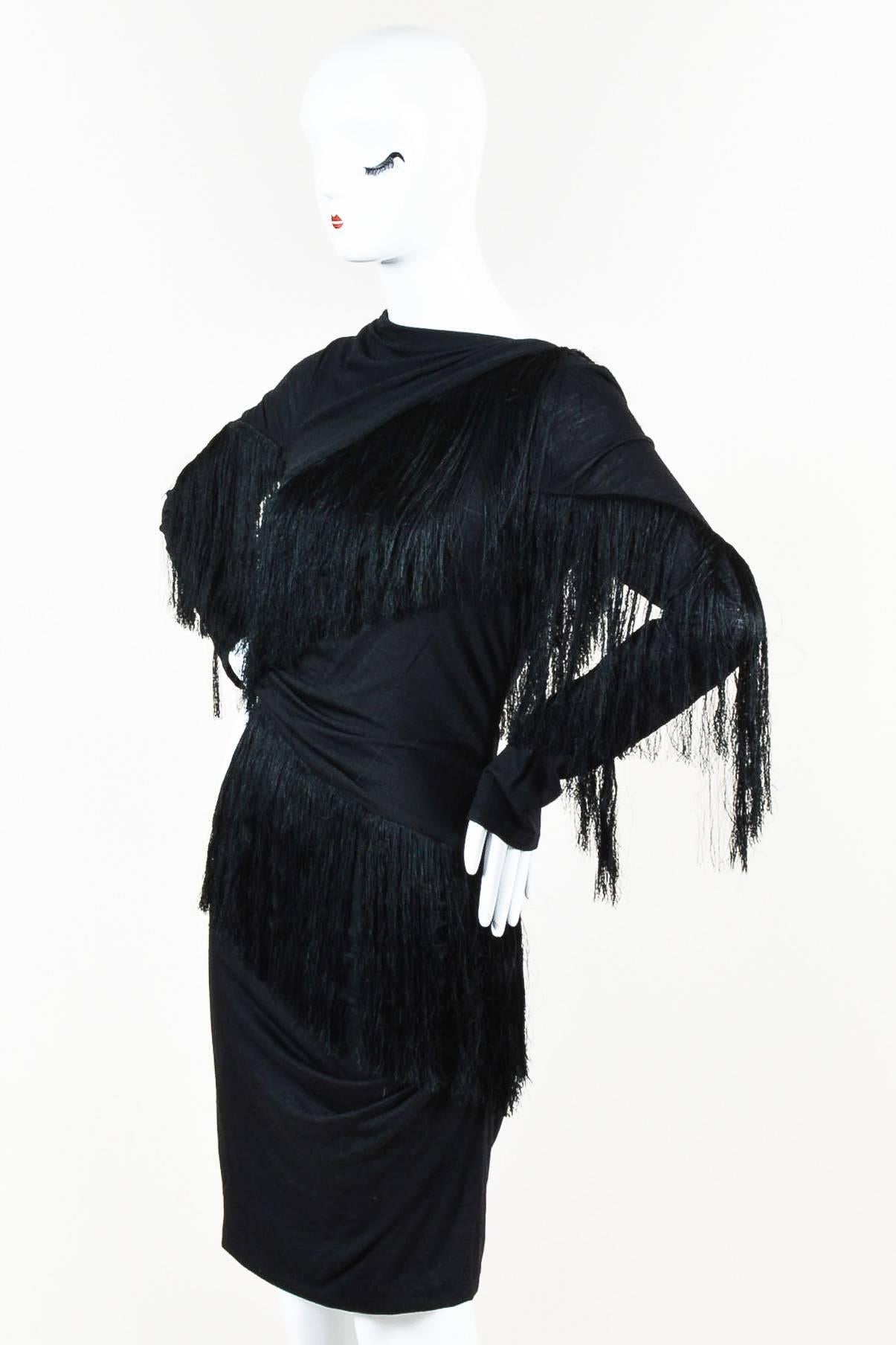 This slinky 'little black dress' was made for cocktail hour. Constructed of a soft and stretchy jersey textile. Long, fine fringe hangs diagonally throughout. Long sleeves. Draped neckline; asymmetric back. Concealed zipper closure at