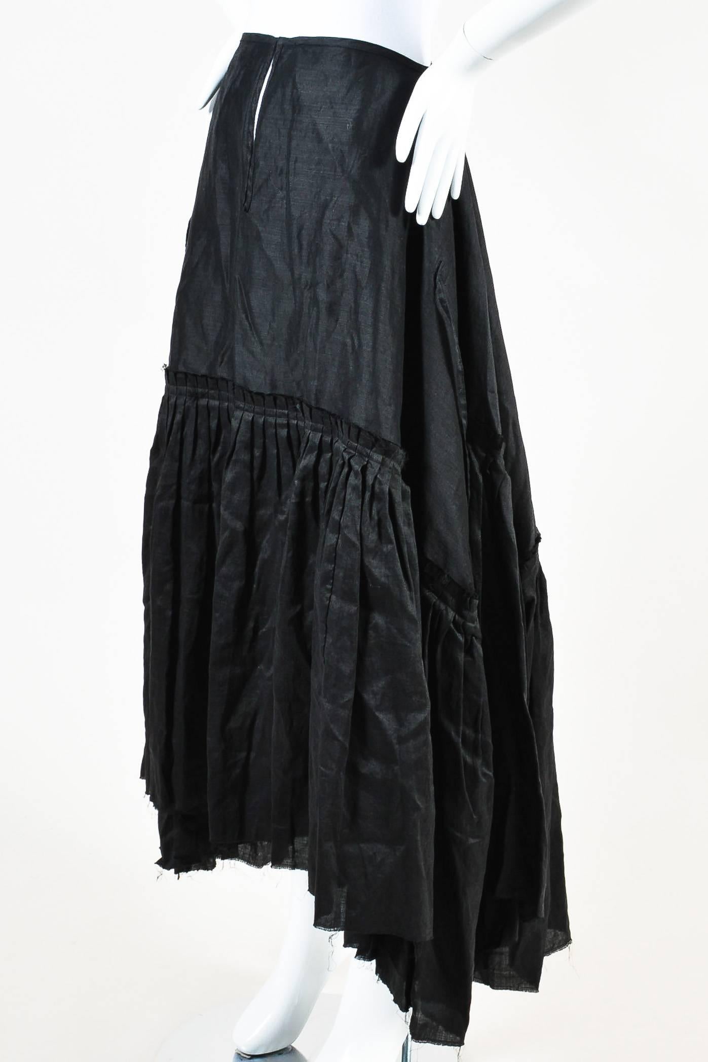 Retails for $965. Dramatic, avant garde skirt. Constructed of black linen. Attached strap details can be tied. Voluminous, tiered pleating with intentionally frayed edges.  Front hook and eye closure with long slit. Unlined. Comes with original tags