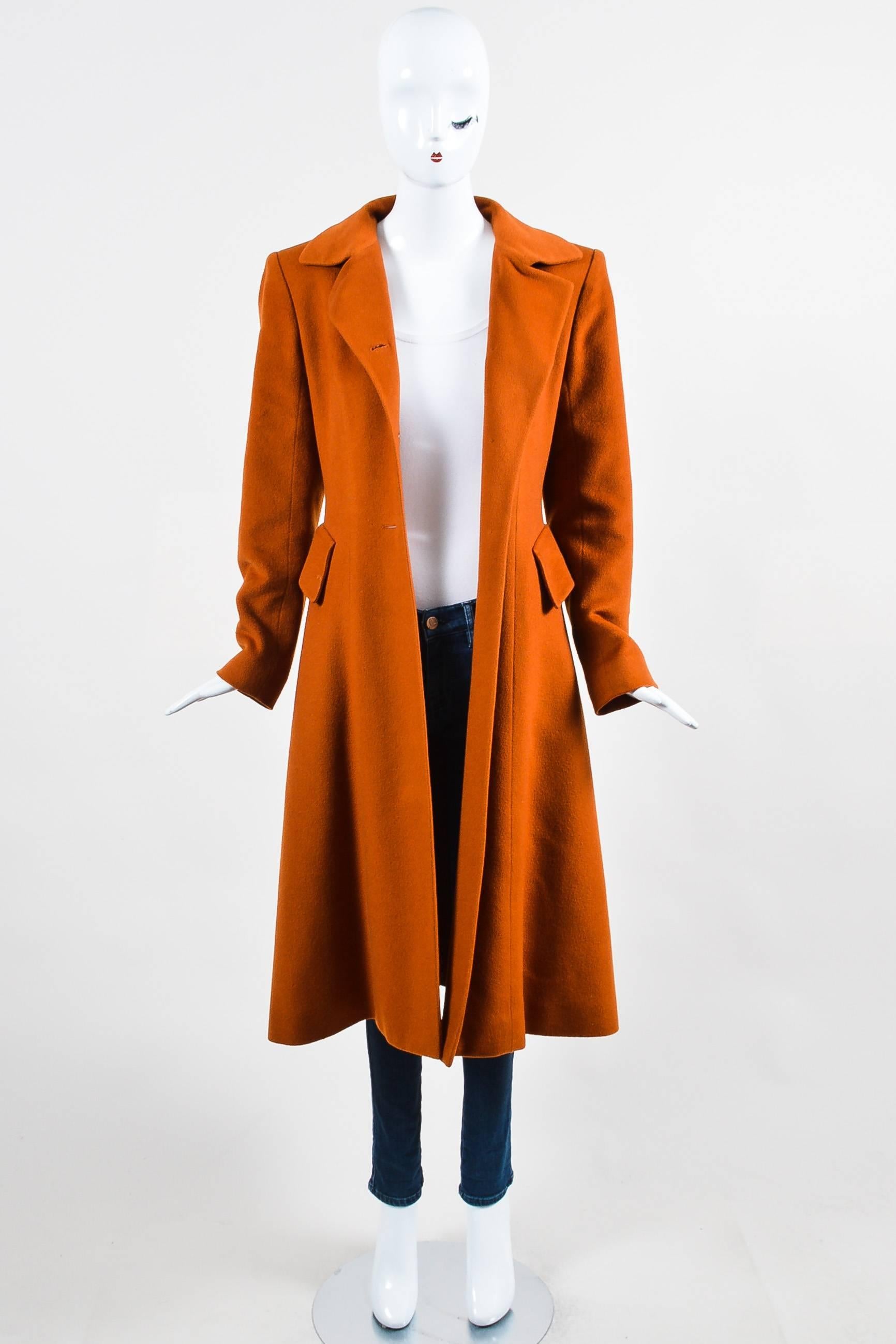 Ladylike overcoat constructed of burnt orange cashmere. Fitted silhouette flares away from the body below waist. Buttons down the front subtly feature the Hermes horse and equestrian. Inset pockets at sides seams with slanted flaps. Tab and hook at