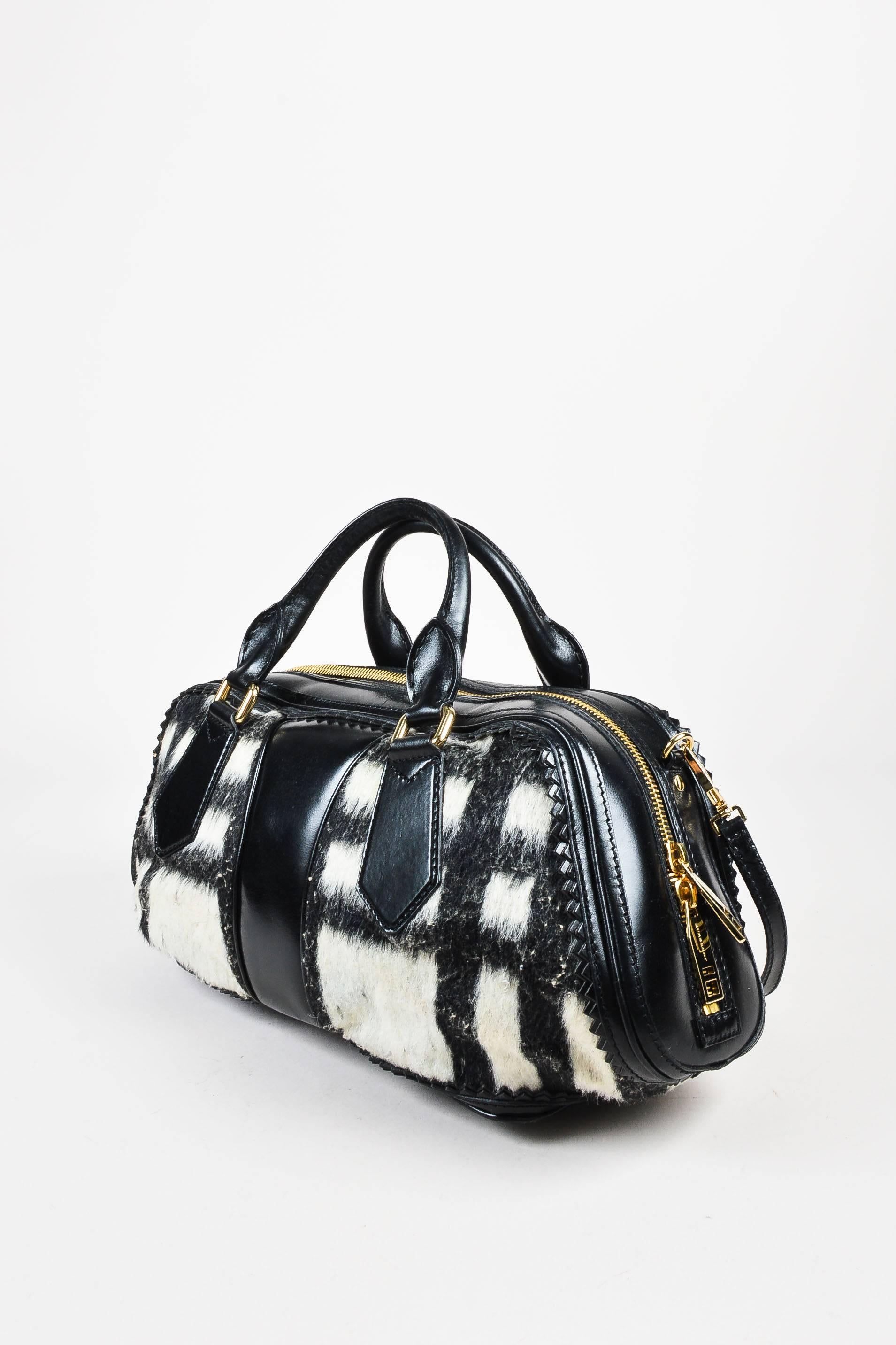 Retails at $2,495. Black and white wool bowling bag from Burberry Prorsum features a black leather trim. Gold-tone hardware details. Oversized fringe tassels on the front. Triangular perforated edges. Two rounded handles and a removable strap for