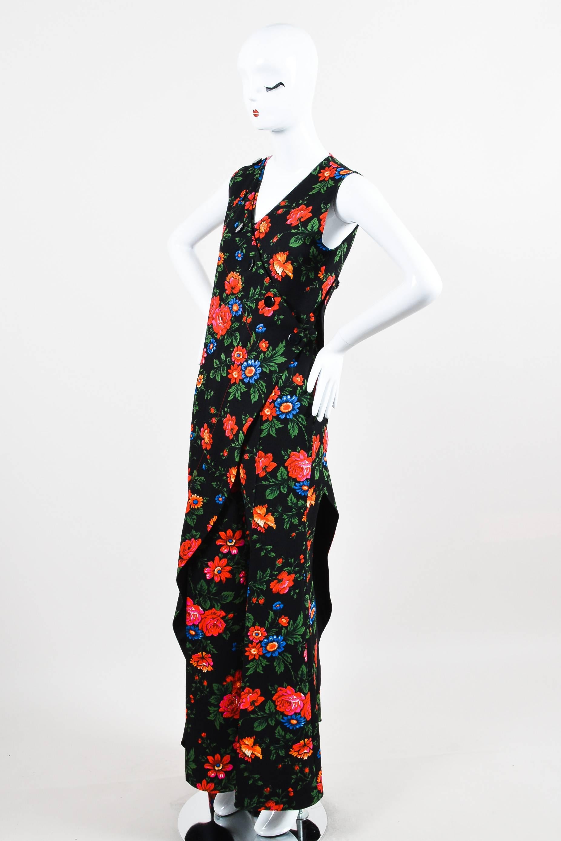 Celine black crepe pantsuit featuring a multicolor floral print pattern and draped, wrap layer along front and back. Designed with shiny button closures and wide legs. Sleeveless. Lined.