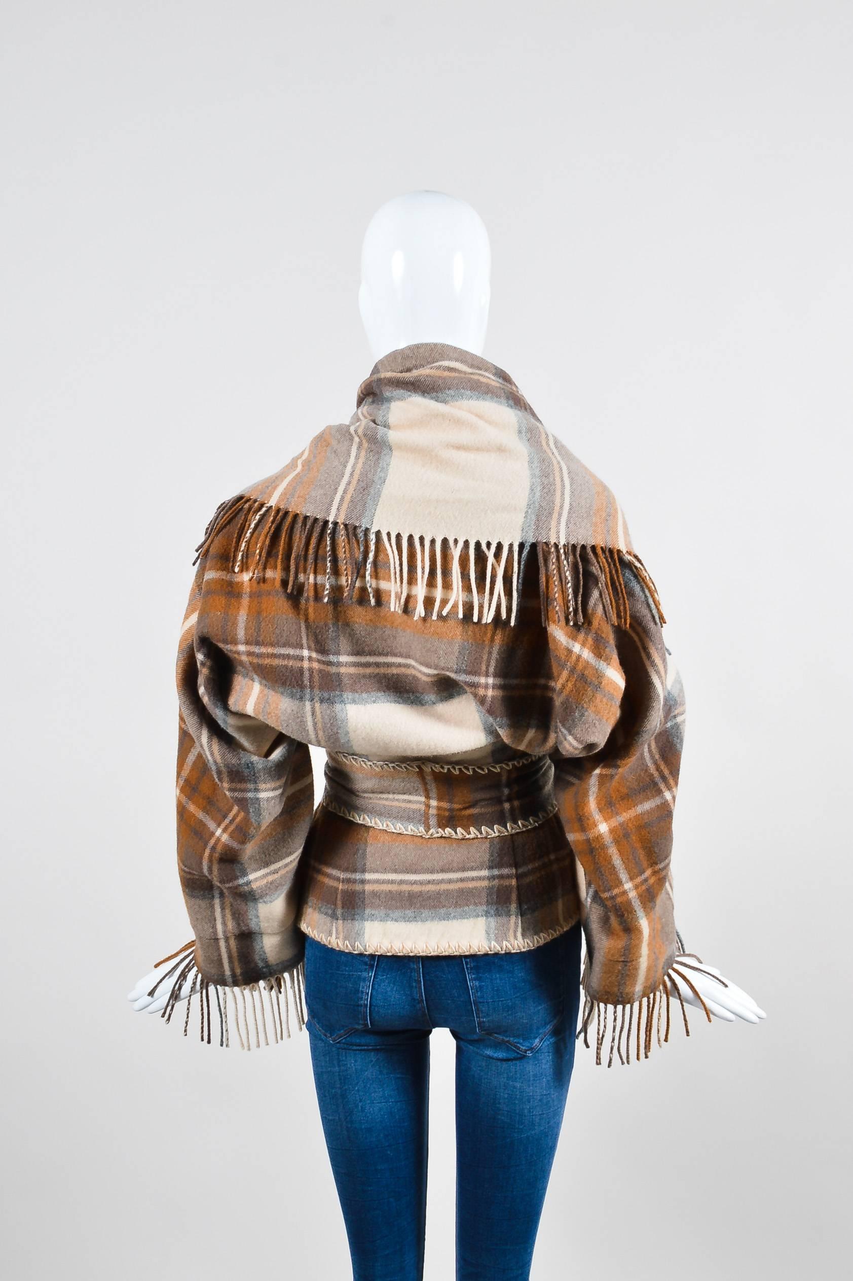 Go southwest chic in this plaid fringed jacket from Alexander McQueen. Brown, tan, and cream colorway in an oversized plaid pattern. Top stitch detailing around the body and belt. Shawl design features a scarf-like neckline that can be pulled up as
