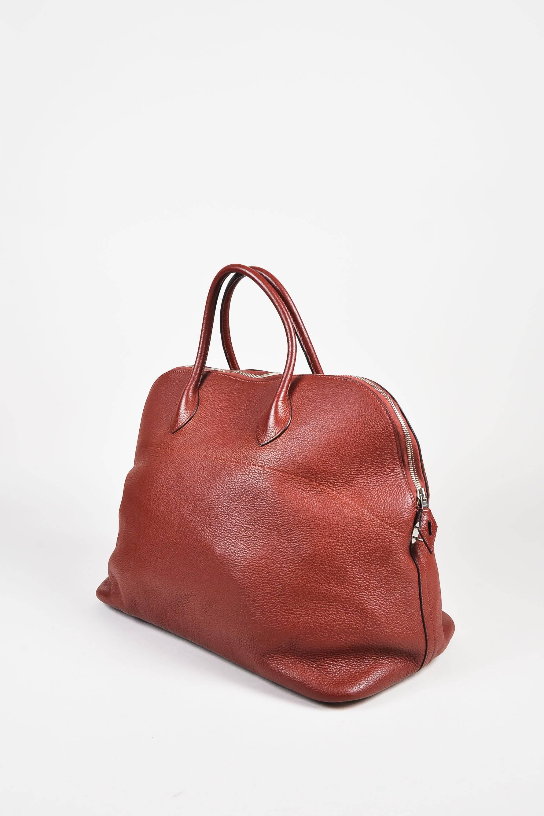 Comes in dust bag. Roomy "Bolide 45" is constructed of Clemence leather in a dark rust red tone. Two rolled top handles and zipper closure. Palladium hardware. Zipper can be secured with lock and keys. Five round feet on bottom help