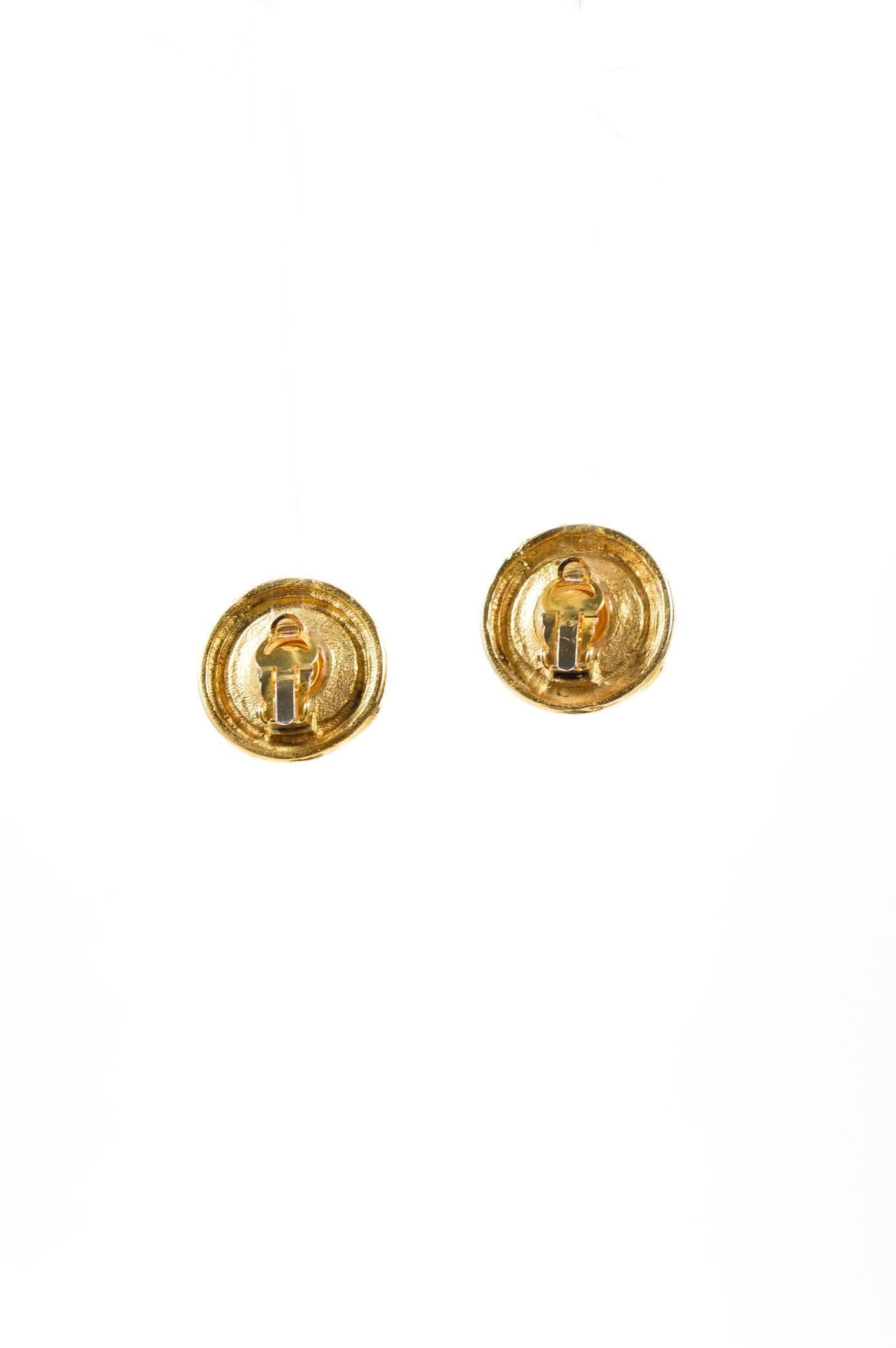 Bright gold-tone circular earrings. Metal is textured to mimic the appearance of braidedrope.Round faux pearlcenter stones.Hinged clip fastening at backs. Flat ovaljewelry tag at backs of earrings read "'C' CHANEL 'R' 'CC' MADE IN