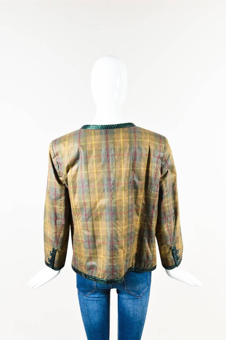 Tan, green, red, and yellow plaid printed cotton long sleeve jacket from Chanel. Green python leather trim. Shoulder pads. Rounded neckline. Gunmetal toned gripoix buttons. Buttons down the front for closure. Four front open pockets with button