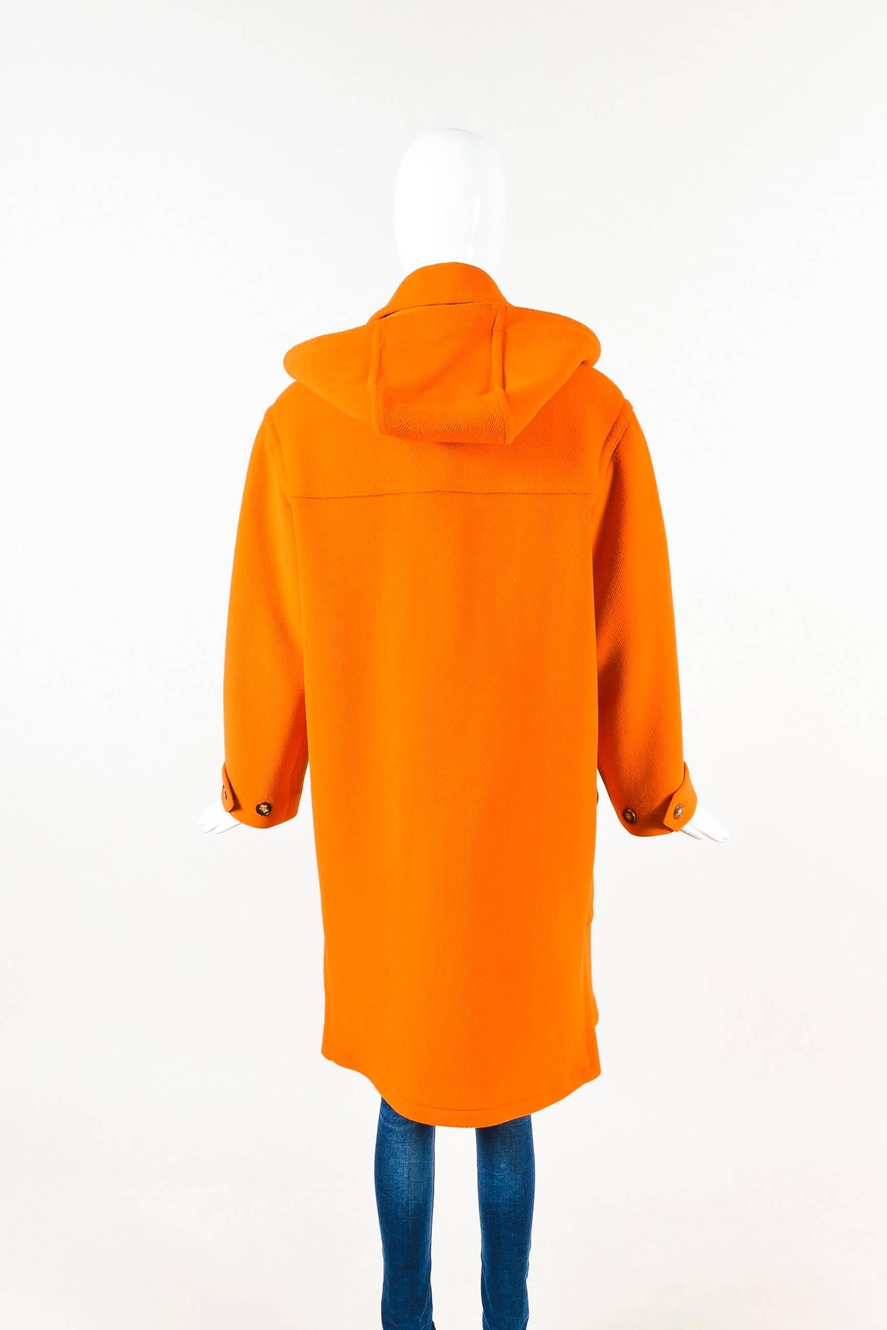 Orange textured wool hooded coat from Hermes. Toggle closures down the front with a brown leather trim. Two front flap pockets. Collar. Hood can be removed, if desired. Short straps on the ends of sleeves with button closures. Slits on the ends of