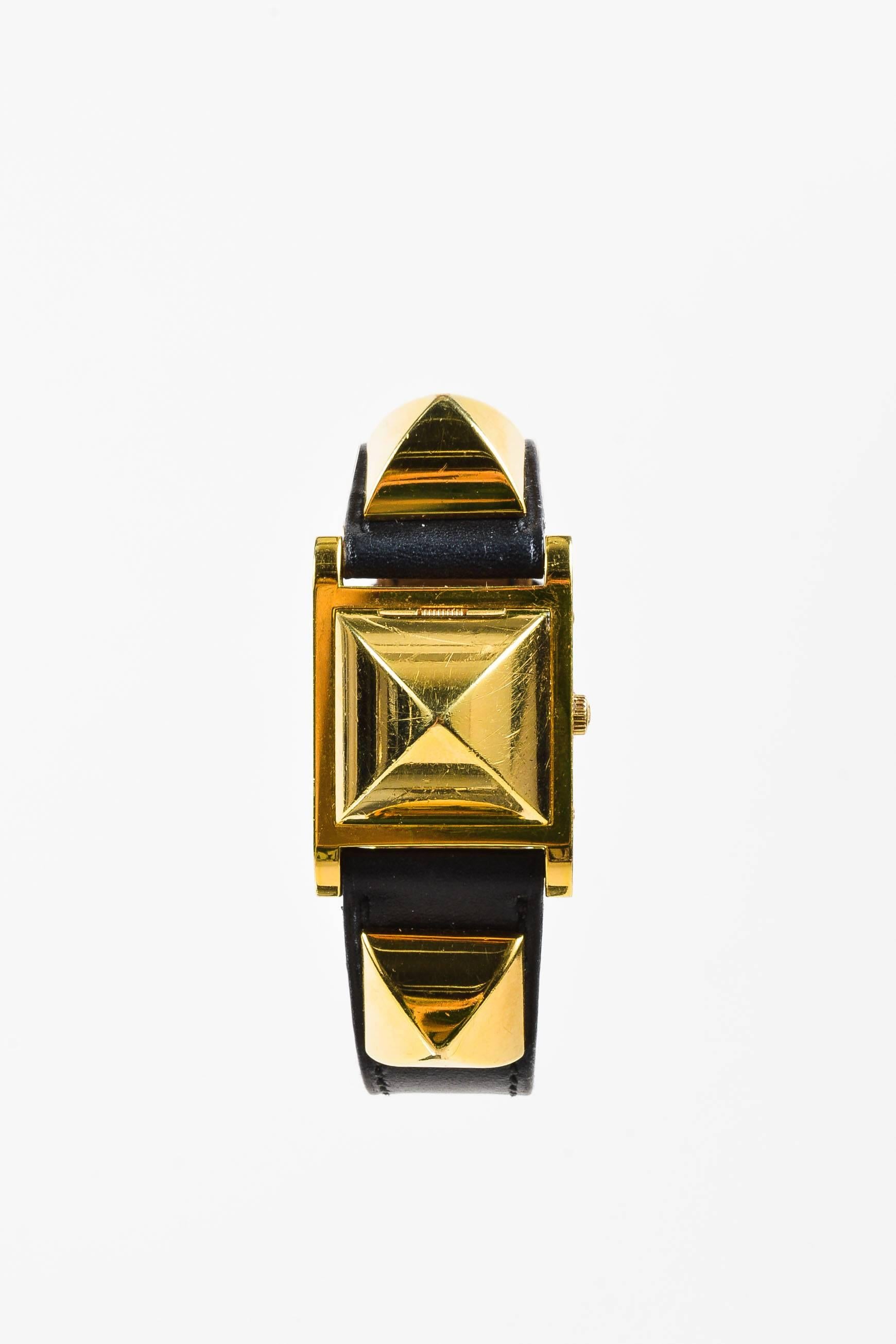 Circa 1995, this unique vintage Hermes watch features a black leather band and gold plated steel construction. The center spiked pyramid lifts up to reveal the watch face with dots at 12, 3, 6, and 9 with two gold-tone hands. Buckle