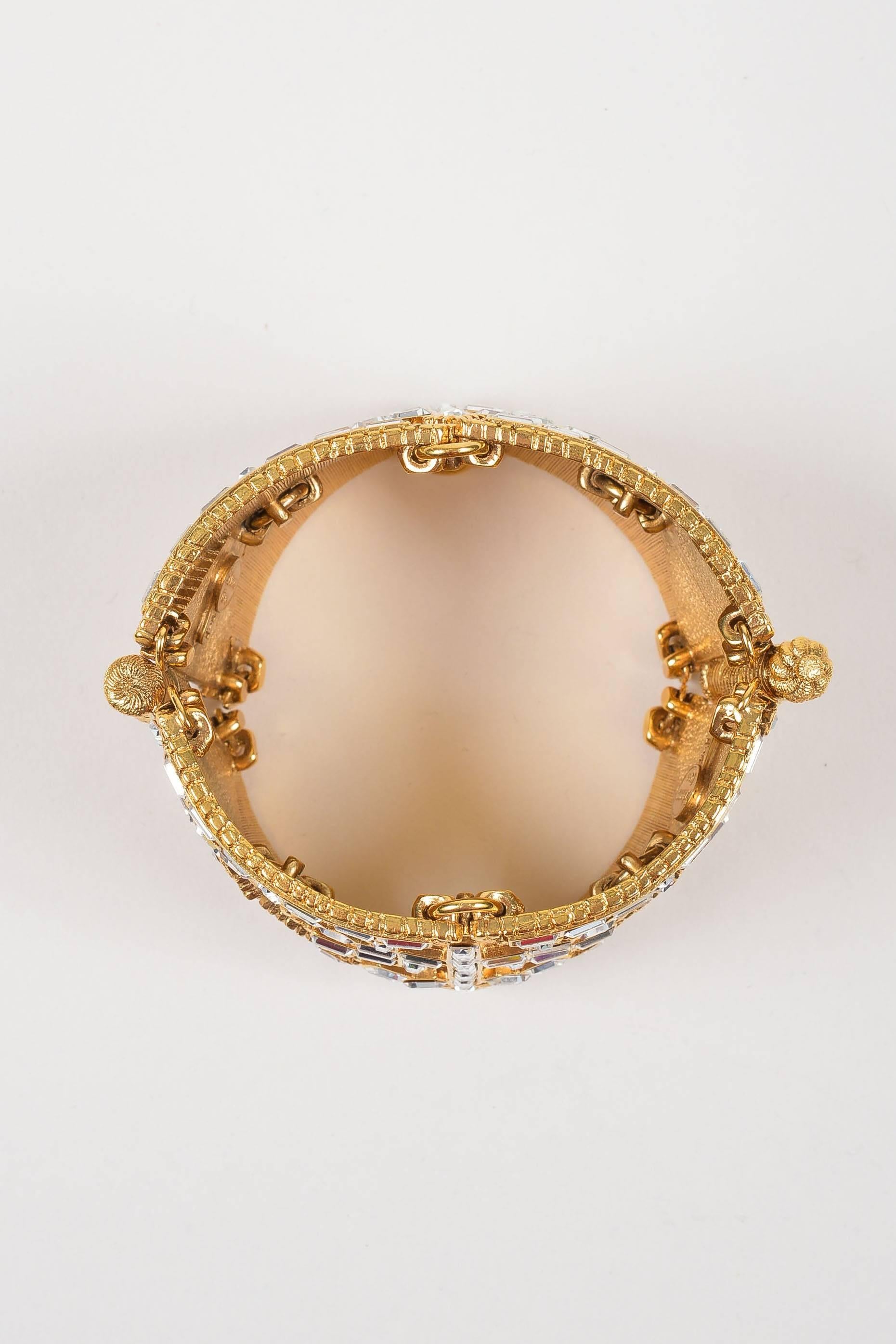 Embellished statement bracelet to make an elegant look stand out. Band is constructed of geometric cut outs connected by o-ring links on interior. Gold-tone plated metal with textured rope pattern throughout. Baguette crystal stones throughout.