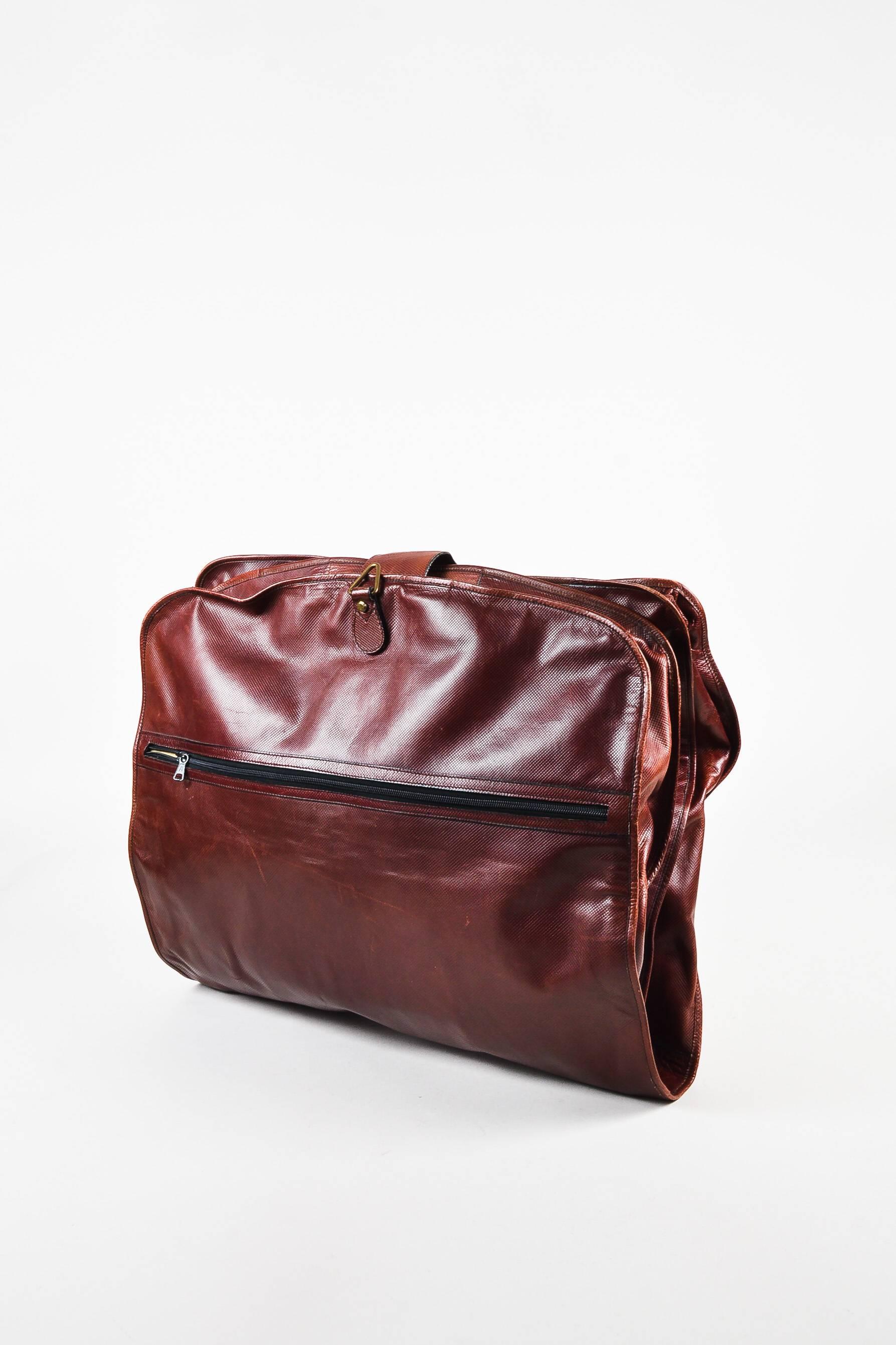 Vintage reddish brown textured leather garment bag from Bottega Veneta features gold-tone hardware details. Bag can be folded shut with snap closures. Wraparound zipper on the front. Push lock closure on the upper front. Comes with lock and keys.