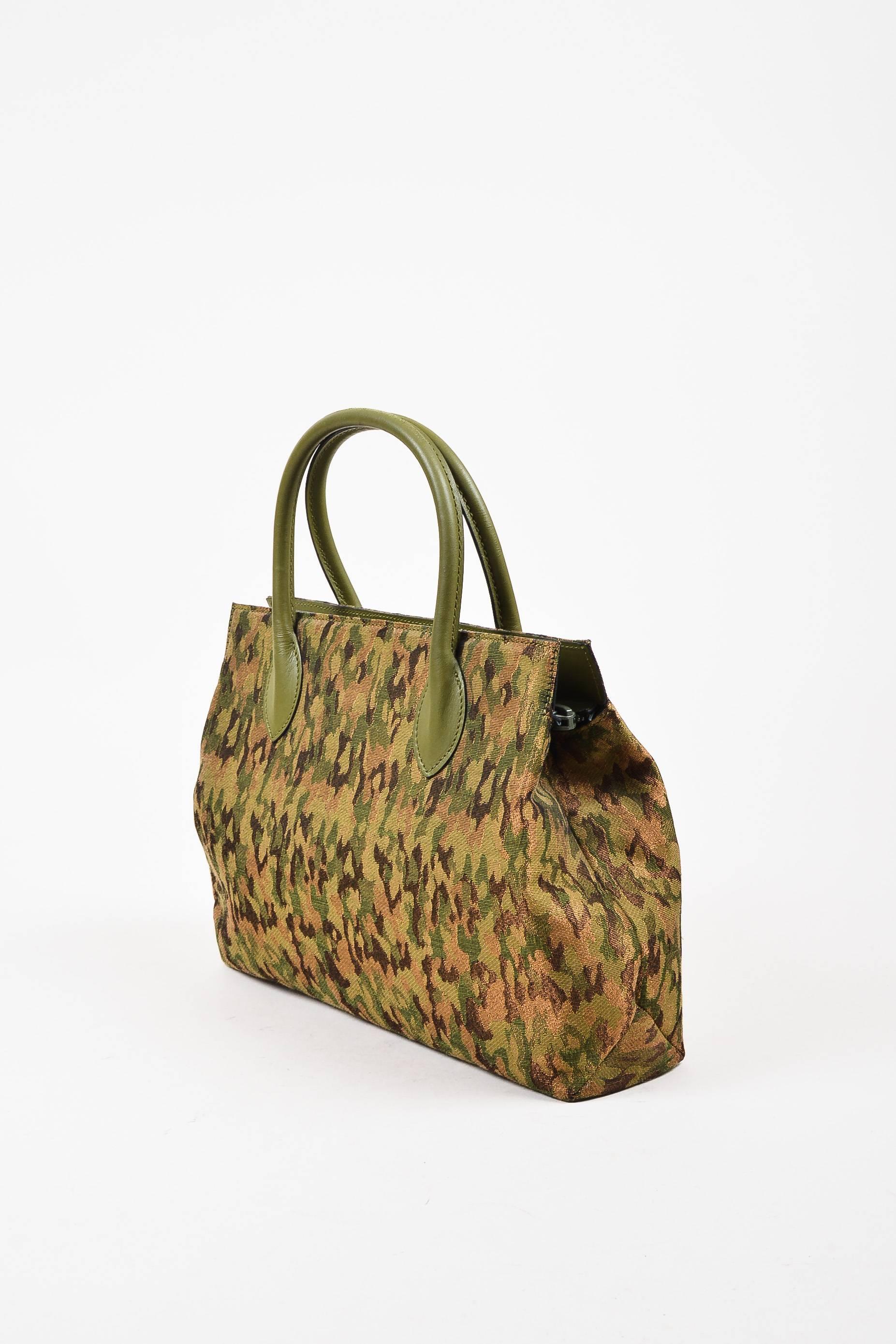 Metallic green, brown, and bronze camouflage printed canvas tote bag from Alaia circa 1990s. Two leather handles. Top zipper for closure. Brown leather interior features a zip pocket. This dainty tote would pair well with a khaki trench coat and