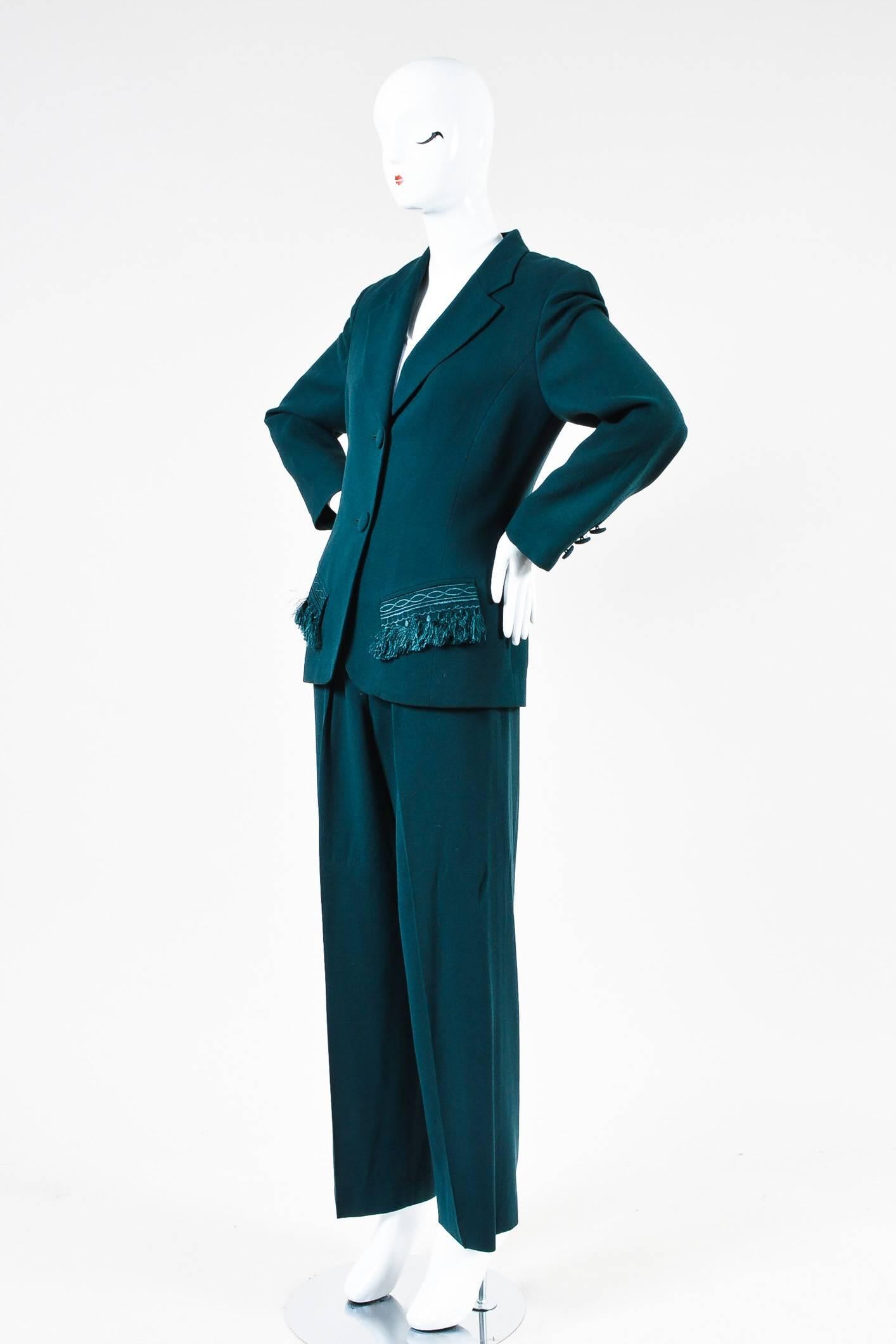 Jacket features a notched lapel, a dual button front, two front flap pockets with fringe trim, buttoned sleeve plackets, and structured shoulders. Pants feature creased legs, pleating, two front pockets, and wide legs.