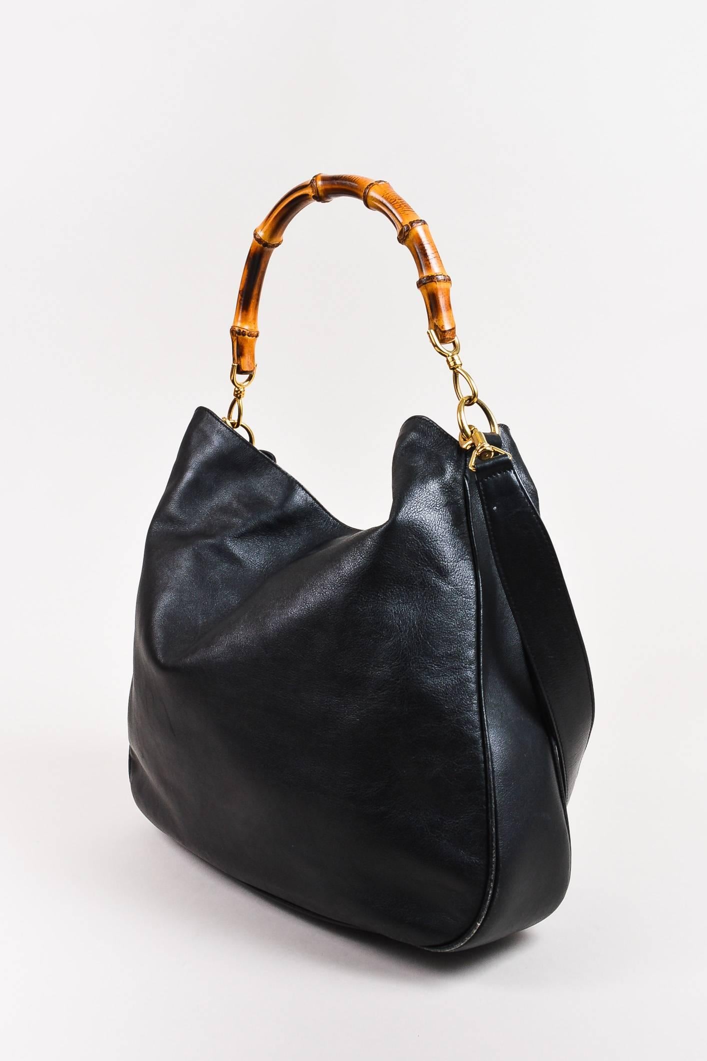 VINTAGE black leather, two-way bag by Gucci. Features a brown bamboo handle and a removable shoulder strap. Gold-tone faux lobster claws at base of both straps. Magnetic snap closure at top.

Interior features: Large zipper pocket

Additional