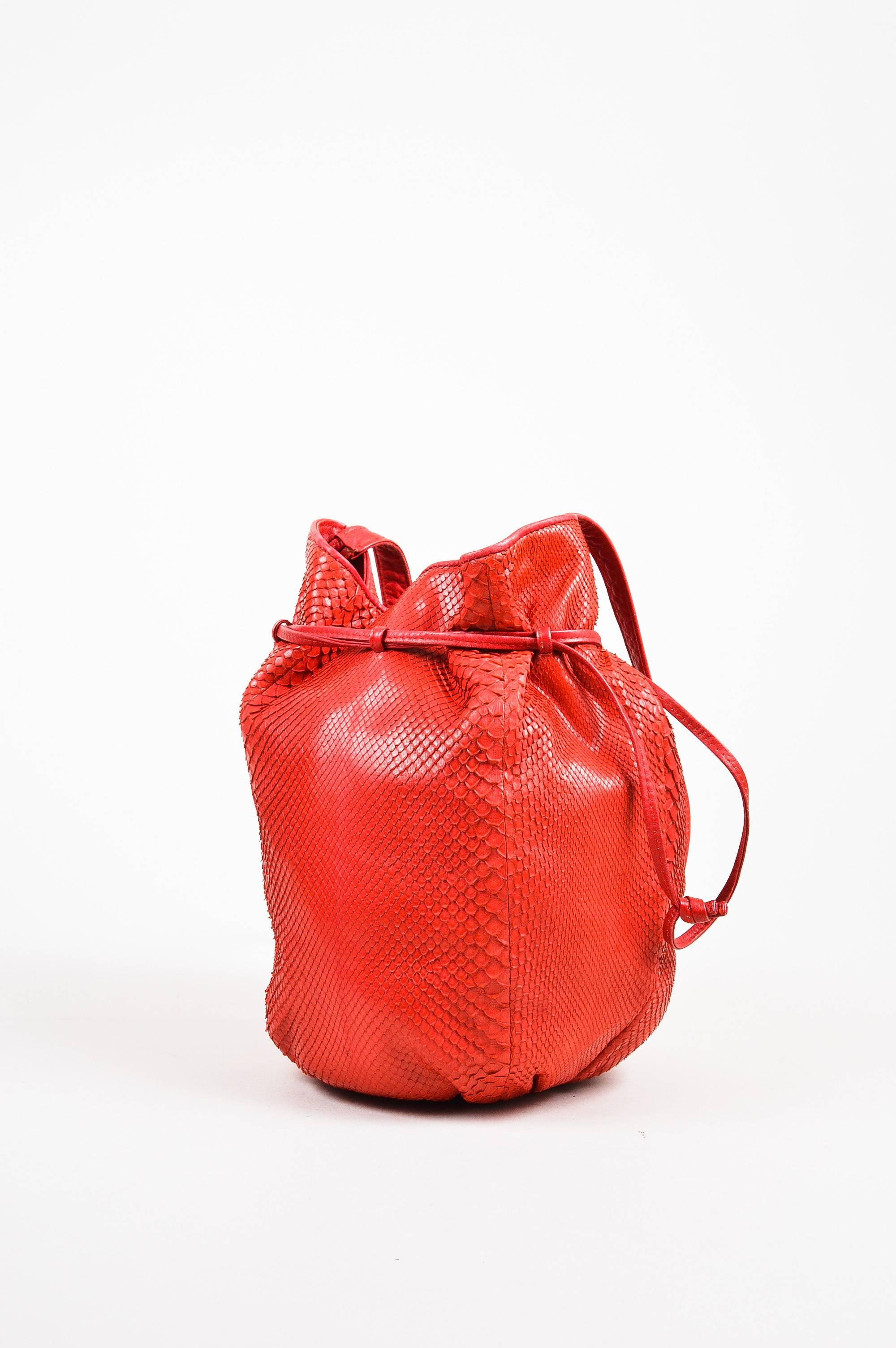 This brightly colored bag would pair well with a black chunky knit sweater and dark wash skinny jeans. Comes with a mirror. Red genuine snakeskin leather bucket bag from Bottega Veneta. Drawstring ties along the upper edge. Single strap for wear.