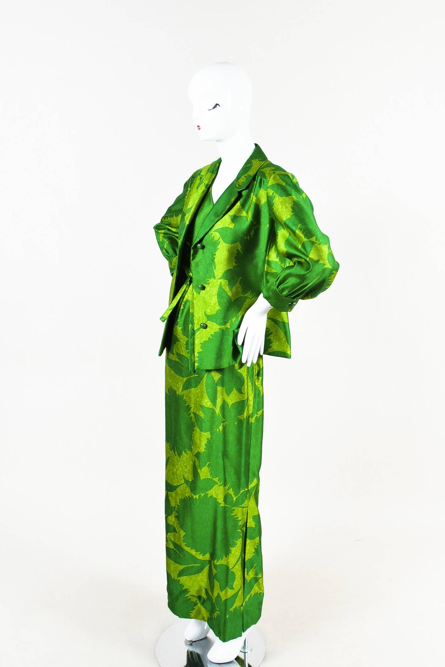 From Nina Ricci's "Mademoiselle Ricci" line, a demi-couture brand developed by the fashion house in the 1960s. Green floral printed jacket and dress set from Mademoiselle Ricci. Sleeveless maxi dress comes with an adjustable tie belt. Slit