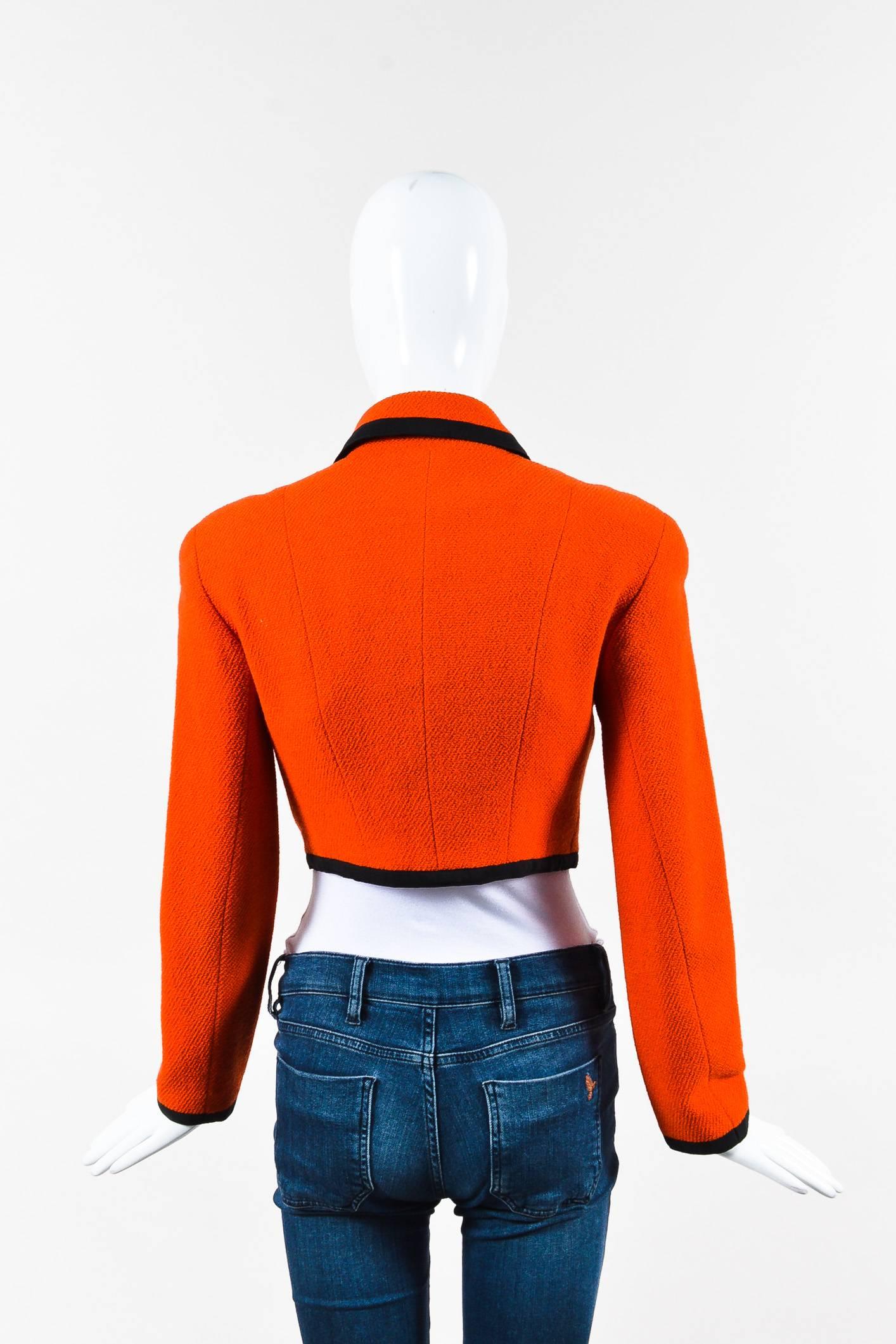Orange wool, cropped long-sleeve jacket by Chanel Boutique. Features chest pockets, gold-tone 'CC' button-up closure, and black grosgrain ribbon trim. Non-removable shoulder pads. Orange silk lining.

Additional measurements: Sleeve Length 23