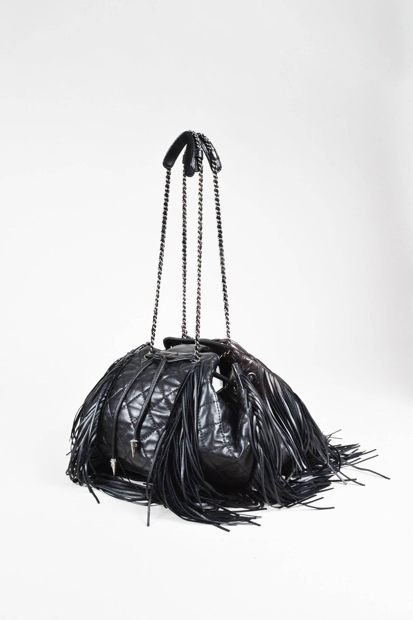 Comes with dust bag and autentication card. Black quilted lambskin leather "Paris-Dallas" drawstring bucket bag from Chanel circa 2014 features layers of fringe. Circular base. Drawstring ties at the upper front with silver-tone spikes at