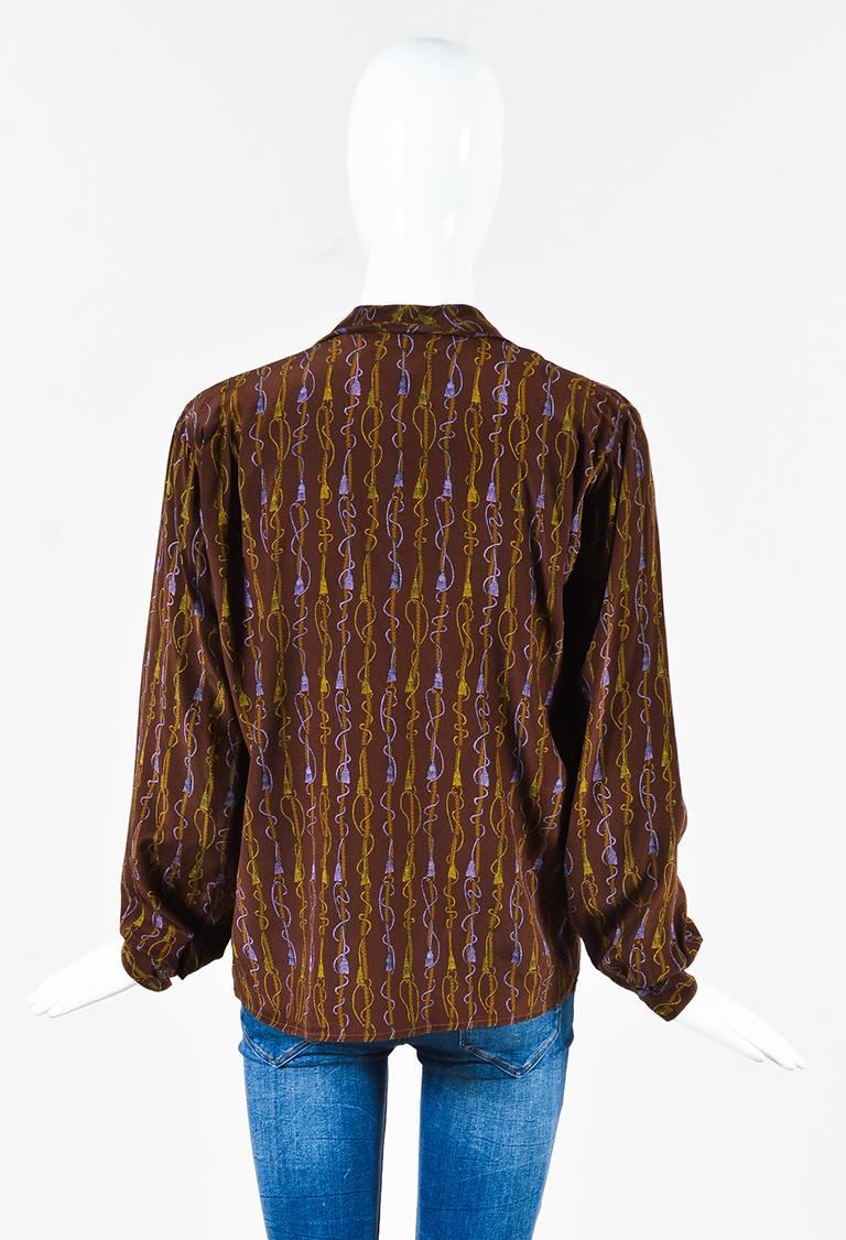 Size: 42 (IT)
Color: Brown,
Made In: Italy
Fabric Content: Silk
Item Specifics & Details: Brown, purple, and yellow silk tassel printed long sleeve collared button up blouse from Gucci. Lapels. V-cut neckline. Cuffs on the ends of the sleeves with a