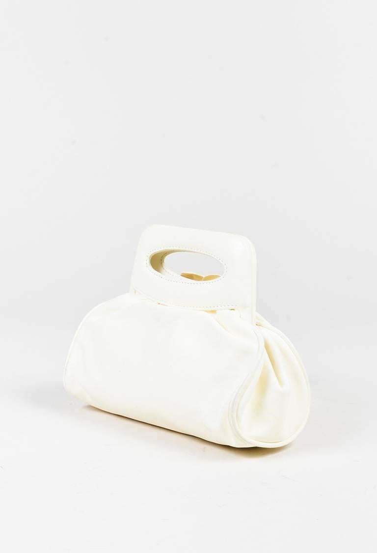 Leather bag featuring a cutout top handle, frame opening, tonal stitching, and a camellia flower at front. Interior features an open wall pocket. Released circa 2003-2004. Serial #: 8789140. Comes with box.

Color: Cream,
Made in: France
Fabric