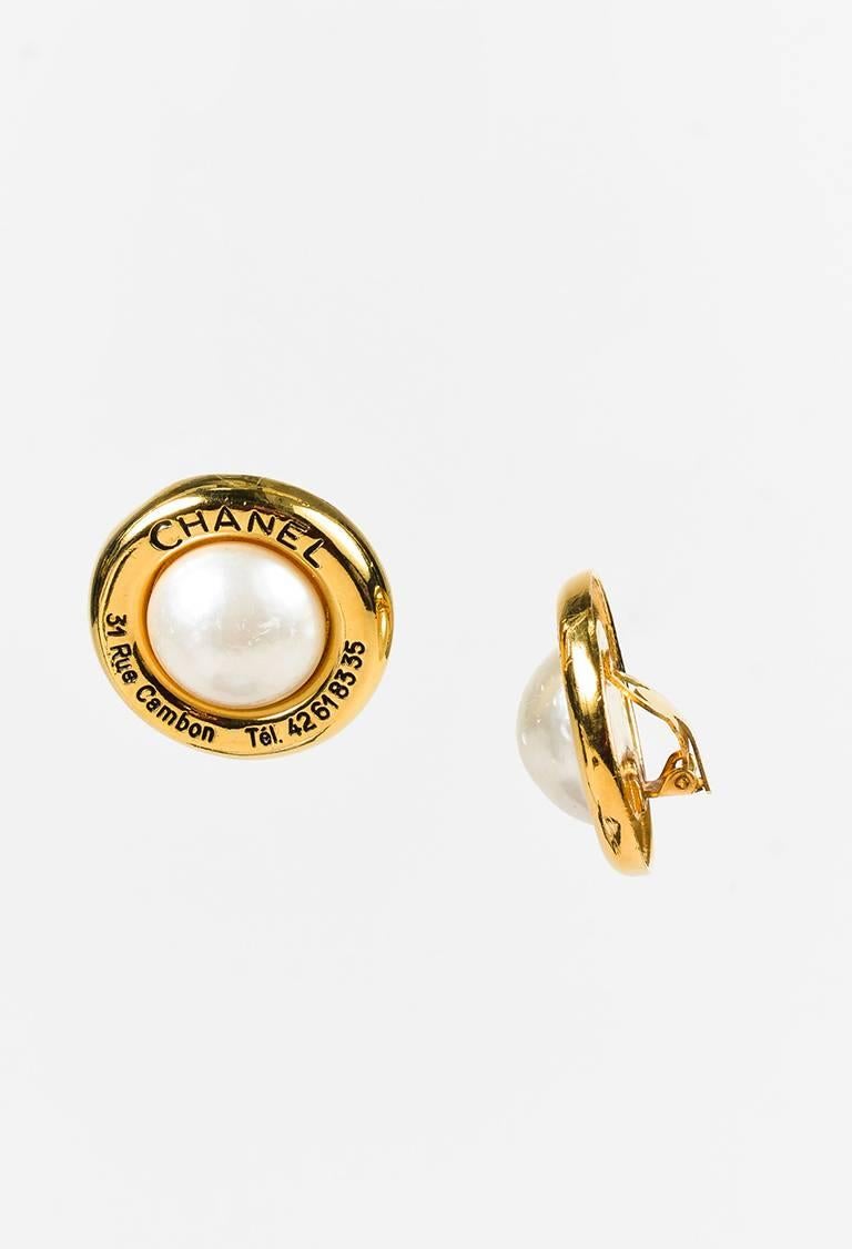 Gold-tone metal earring featuring a center faux pearl, black logo lettering, and a clip-on clasp.

Made in: Unknown
Color: Black, White, Gold
Content: Metal, Faux Pearl
Condition: Pre-owned. Patina at back interiors. Nicks and scratches at faux