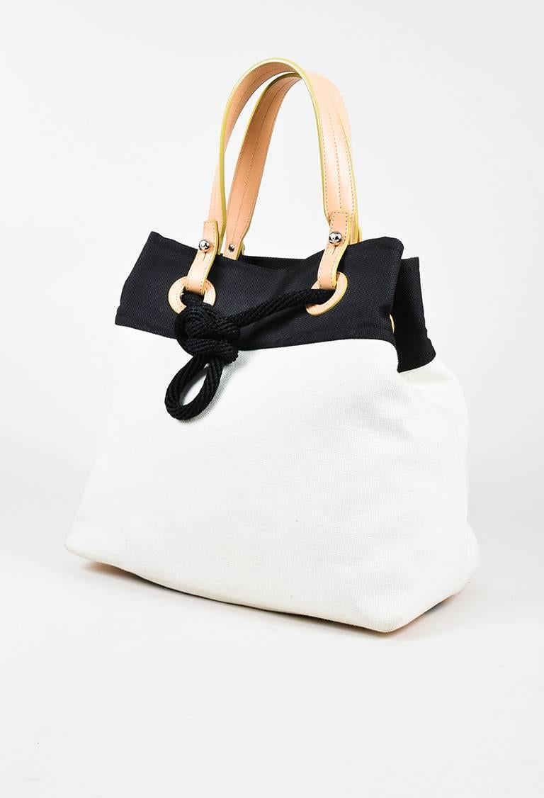 Cream and black canvas nautical tied satchel bag from Chanel circa 2009-2010. Tan leather trim. Four silver-tone bag feet. Nautical tie along the top with a silver-tone lobster clasp closure. Two handles for wear. Interior lining features a zip