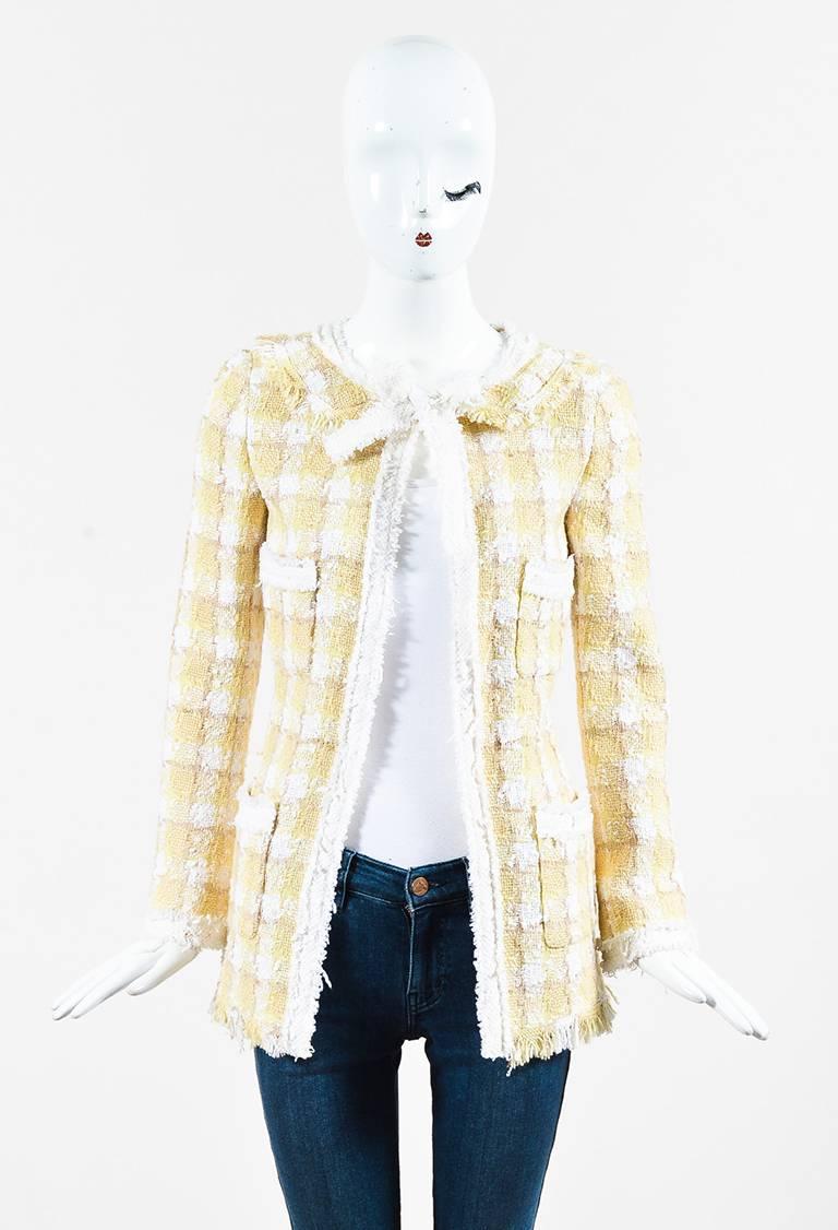 Yellow, white, and beige tweed long sleeve jacket from Chanel circa Resort 2004. Rounded neckline with a tie and button closure at the front. Flat lay collar. Shoulder pads. Four open pockets on the front. Frayed trim. Two 'CC' buttons on the ends