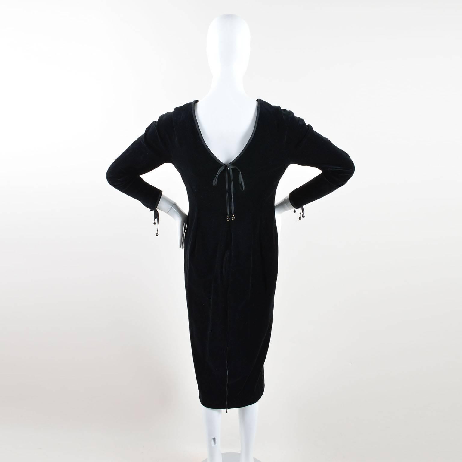 New with tags. Soft black velvet sheath dress. Black grosgrain ribbon trim at neckline and wrists; ribbon trim extends into ties with small round 'CC' logo beads. Midi-length. Long fitted sleeves. Rounded neckline, v-back. Two front hip patch