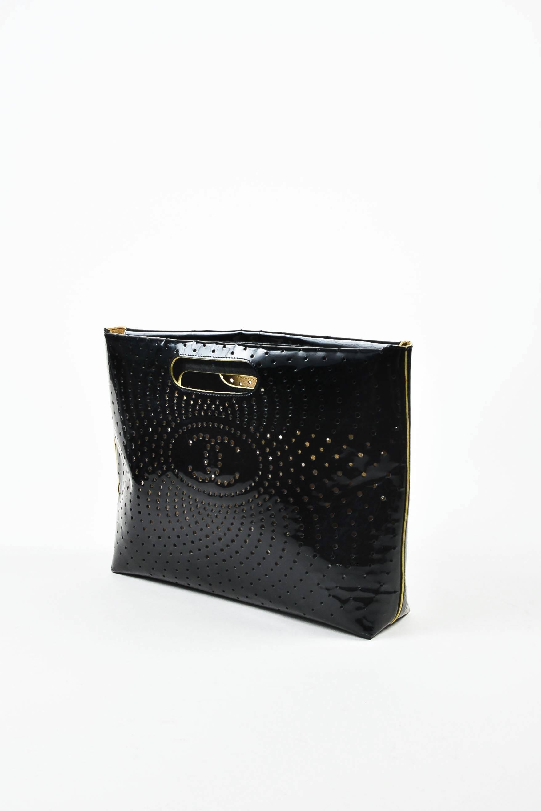 This rectangular shaped clutch handbag by Chanel is constructed of black patent leather. Swirling perforated embellishments throughout with 'CC' logo at the center. Two top handle holes. Bag is open at top. Serial number reads,