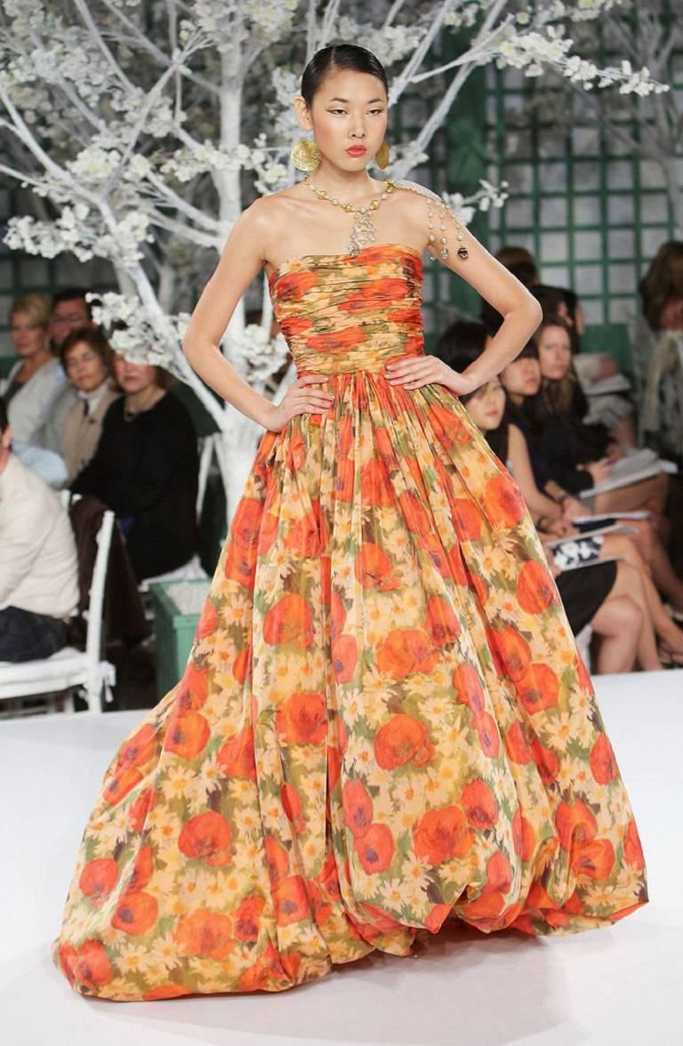 Showstopping ball gown constructed of sumptuous silk. Watercolor floral print throughout in warm-toned shades of red, yellow, and green. Strapless bodice with intricate pleating throughout. Bodice features an interior corset with boning and built-in